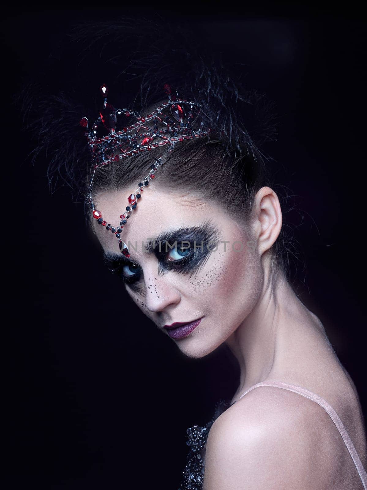 Portrait of the ballerina in the role of a black swan on black studio background. The face close up