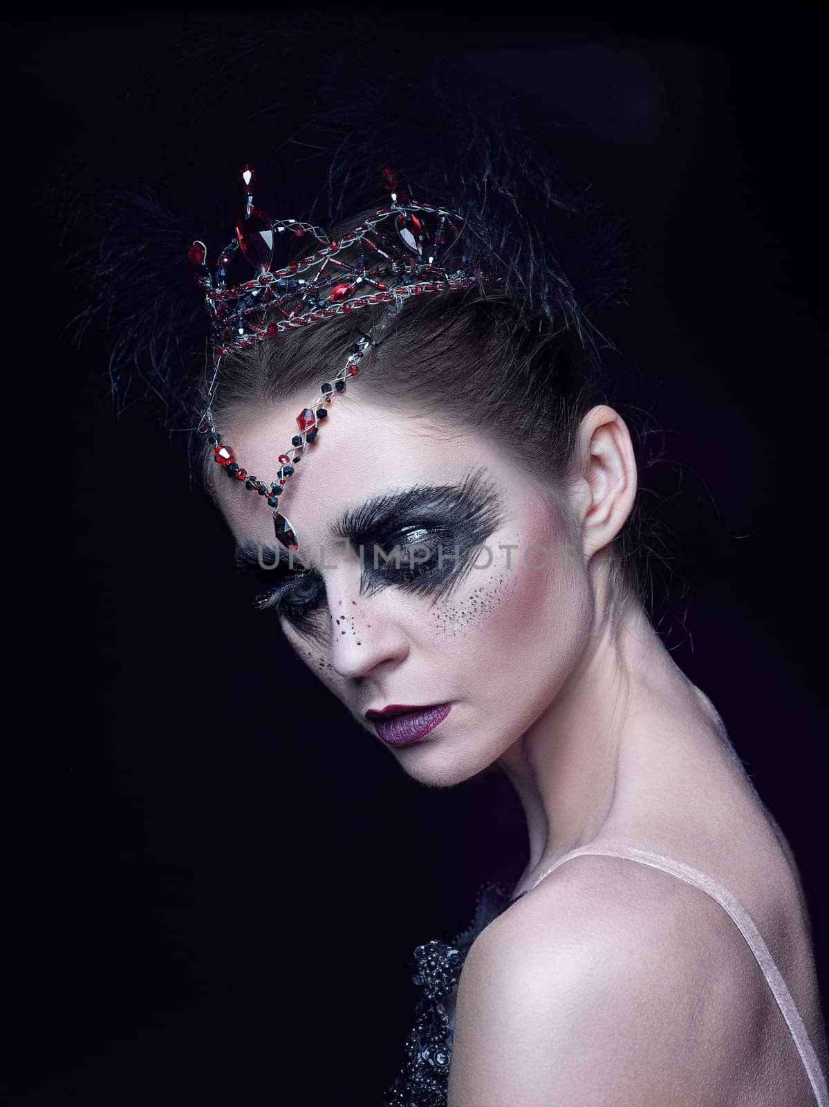 Portrait of the ballerina in the role of a black swan on black studio background. The face close up