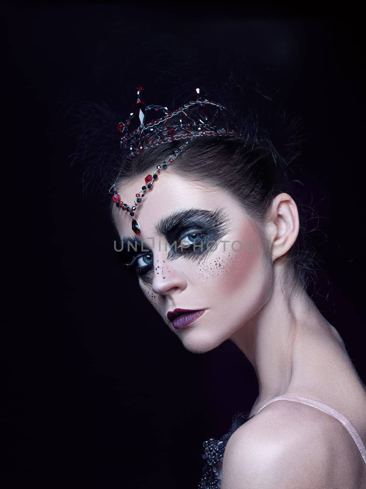 Portrait of the ballerina in the role of a black swan on black studio background. The face close up