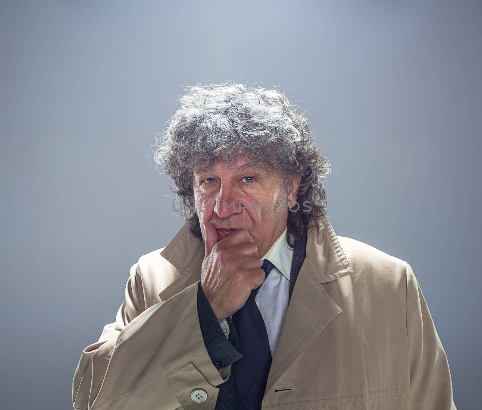 The senior man in cloak as detective or mafia boss. Studio shot on gray in retro stile