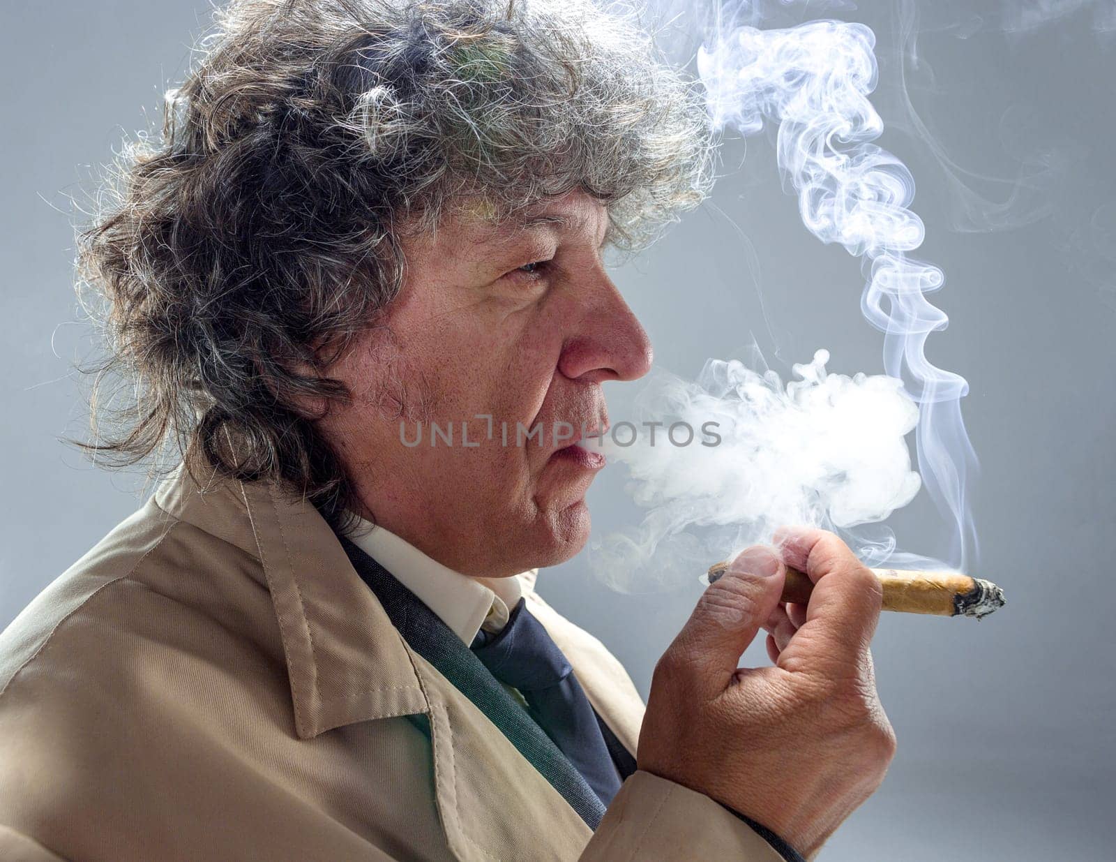 The senior man in cloak with cigar as detective or mafia boss. Studio shot on gray in retro stile