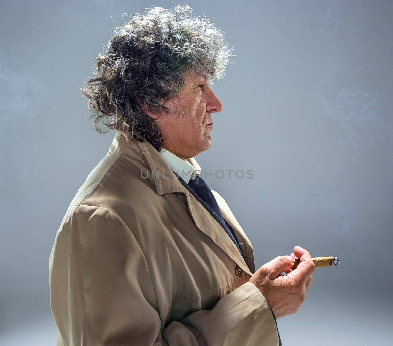 The senior man in cloak with cigar as detective or mafia boss. Studio shot on gray in retro stile
