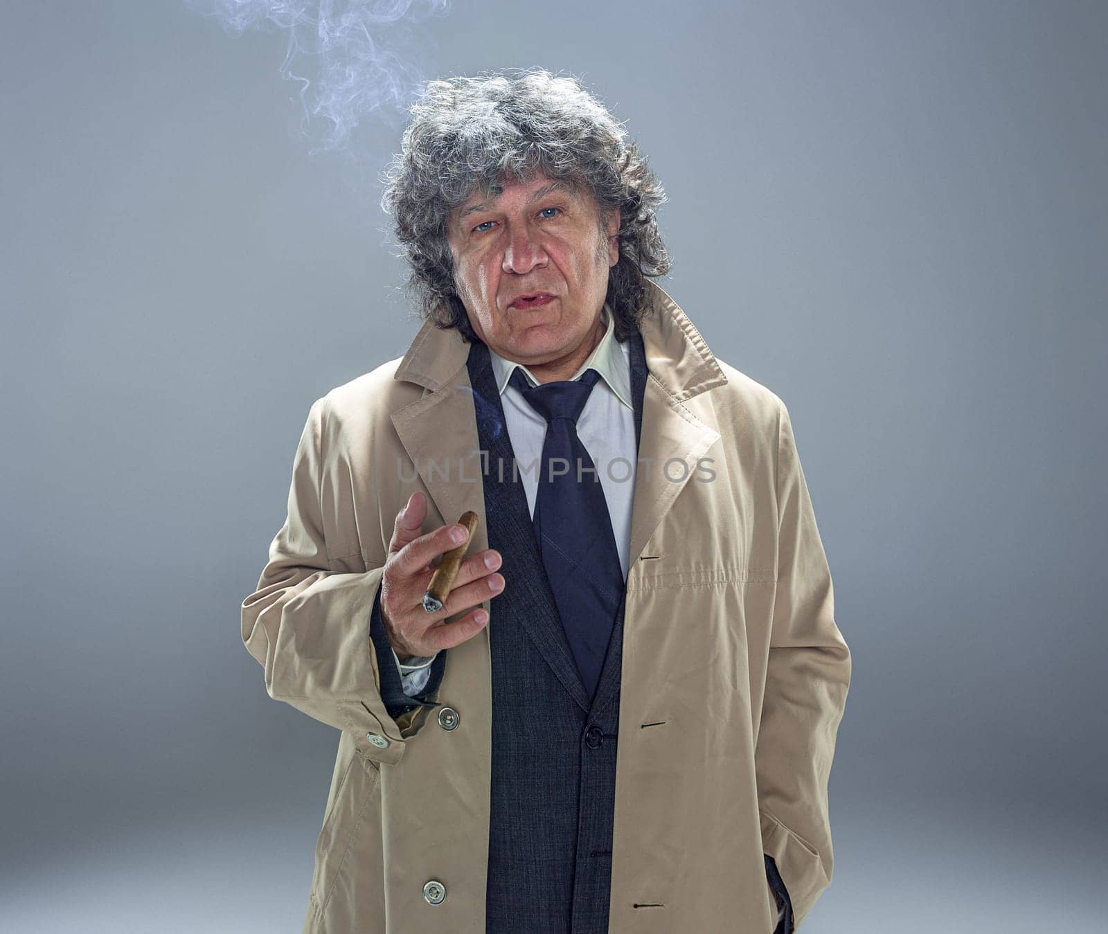 The senior man in cloak with cigar as detective or mafia boss. Studio shot on gray in retro stile