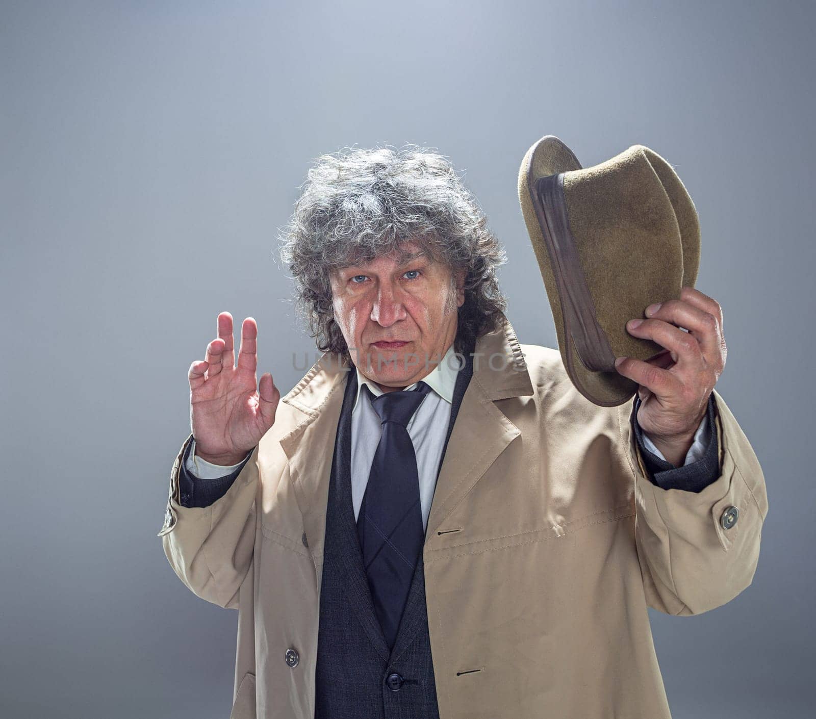 The senior man in cloak as detective or mafia boss. Studio shot on gray in retro stile. Mature man with hat and suitcase