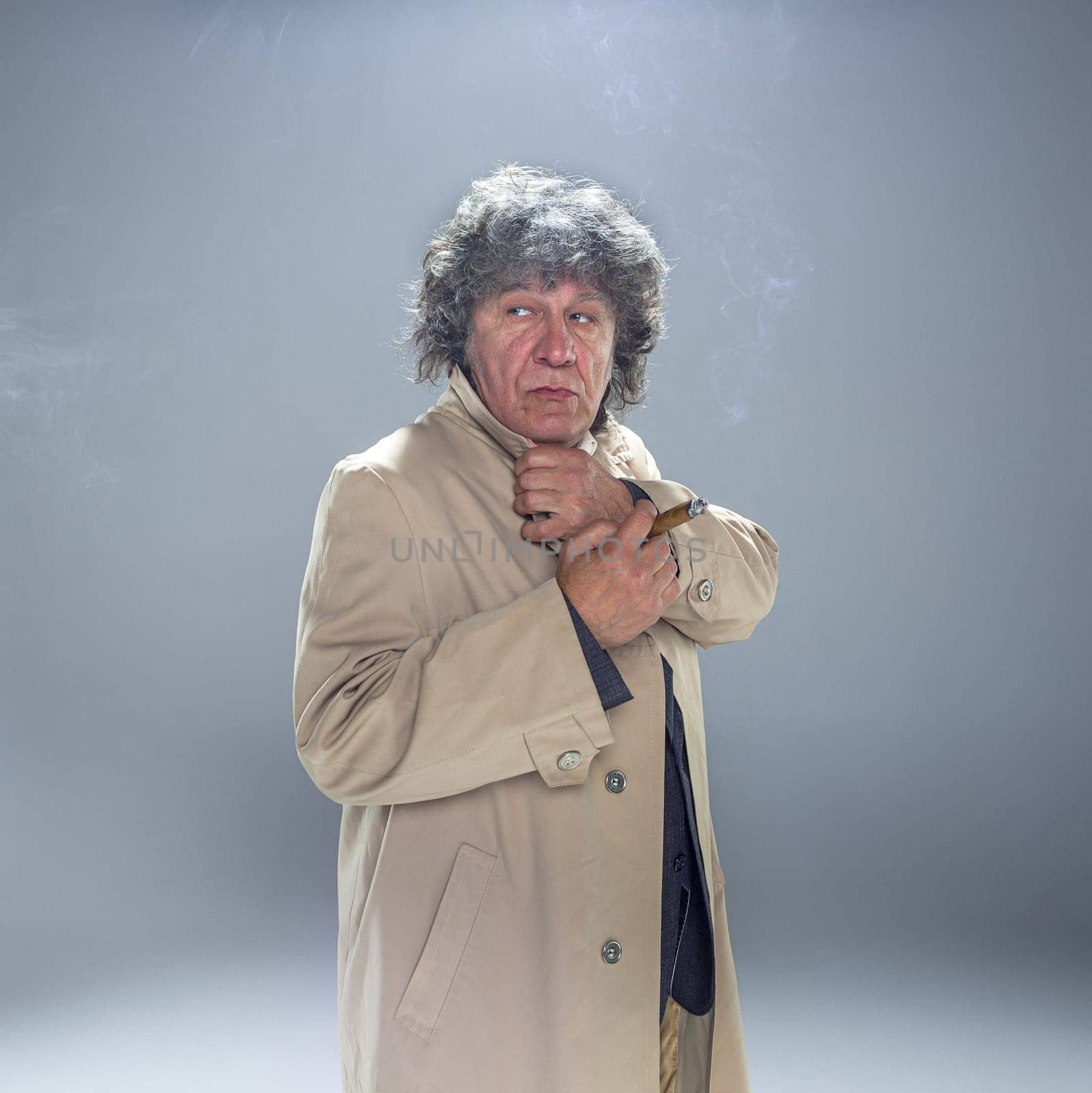 The senior man in cloak with cigar as detective or mafia boss. Studio shot on gray in retro stile