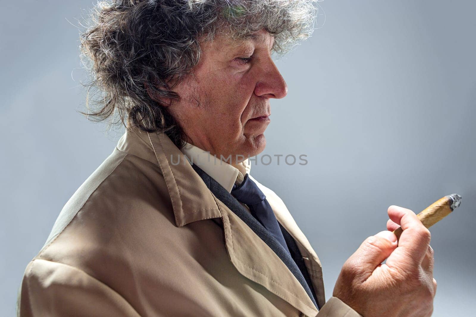 The senior man in cloak with cigar as detective or mafia boss. Studio shot on gray in retro stile