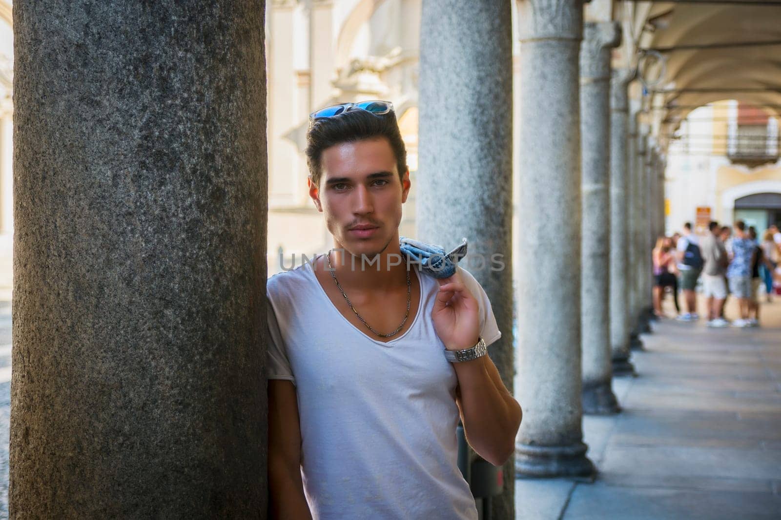 Handsome young man standing outdoors under old colonnade in european town or city