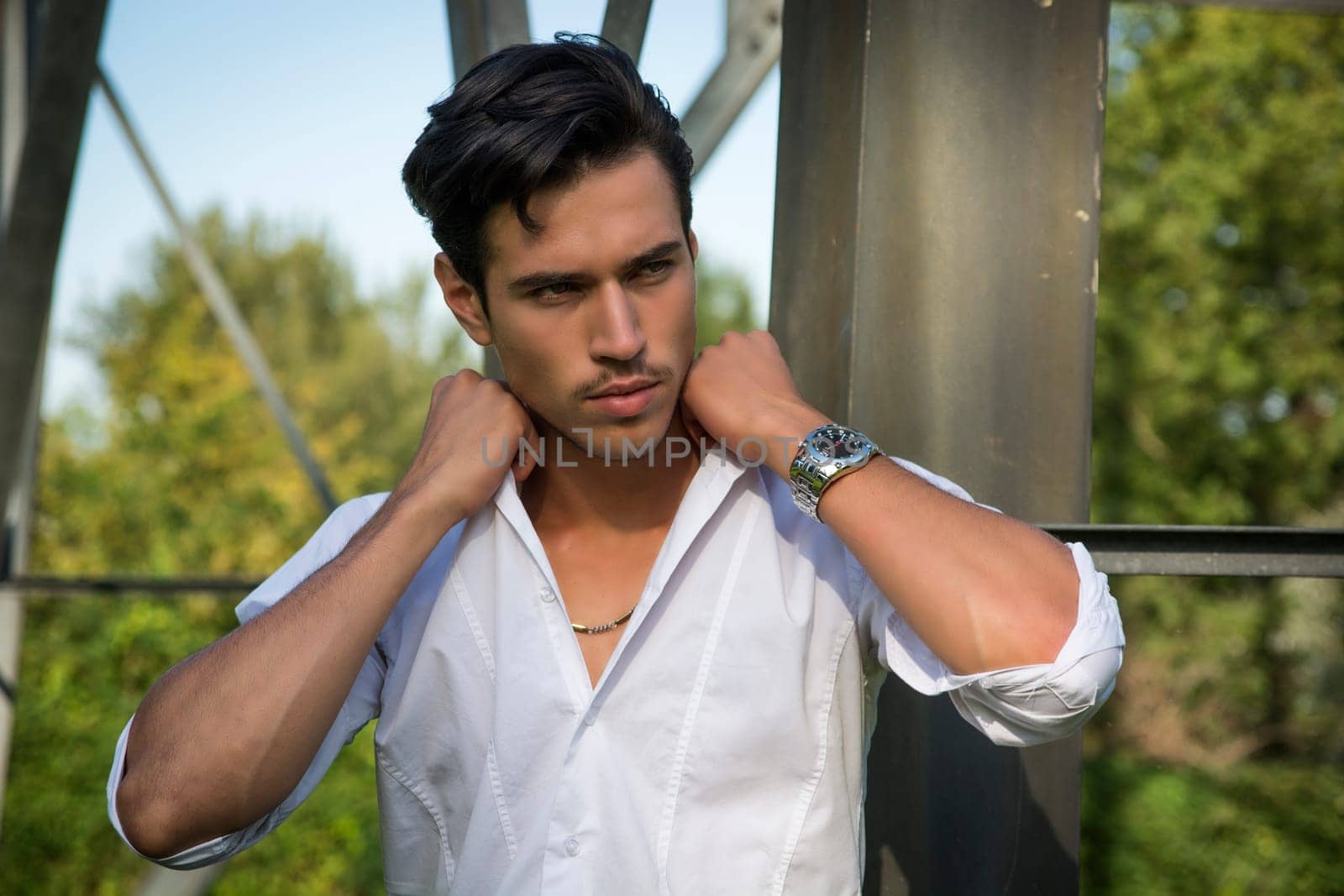 Handsome young man leaning against metal electricity trellis, looking away