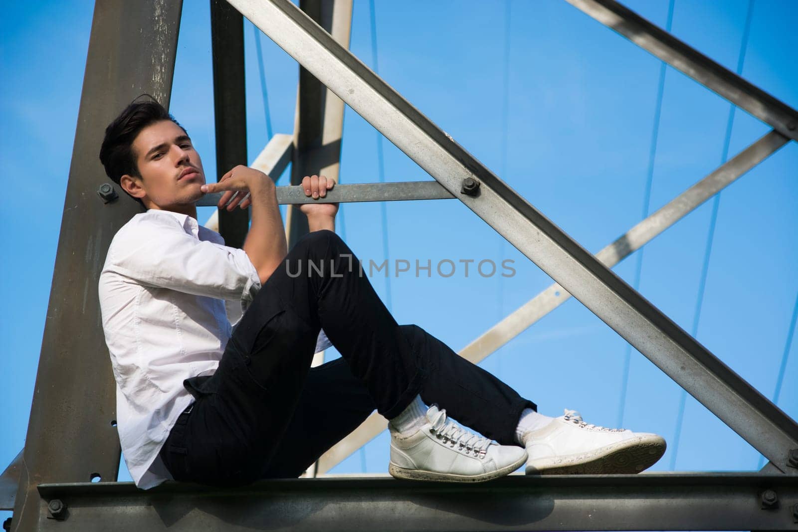 Handsome young man sitting on metal electricity trellis, looking at camera