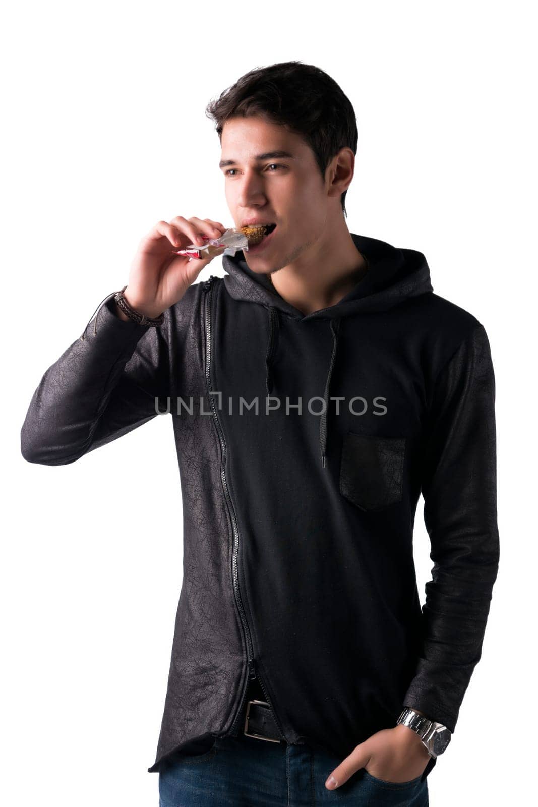 Handsome young man eating cereal bar, looking away standing, isolated on white background