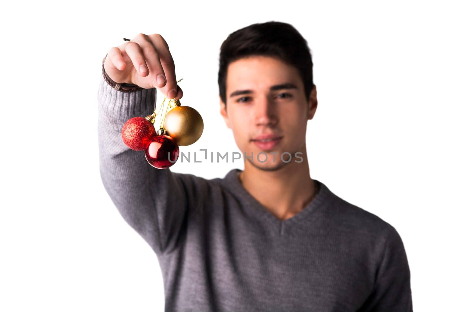 Handsome young man holding Christmas tree balls in front of his face, looking at camera on white background