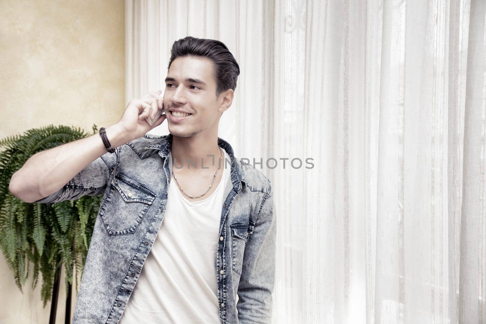 Handsome young man talking on telephone at home, smiling and looking to a side