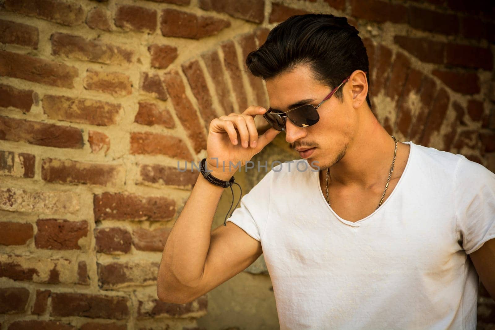 Handsome young man with sunglasses and white t-shirt, outdoors next to brick wall