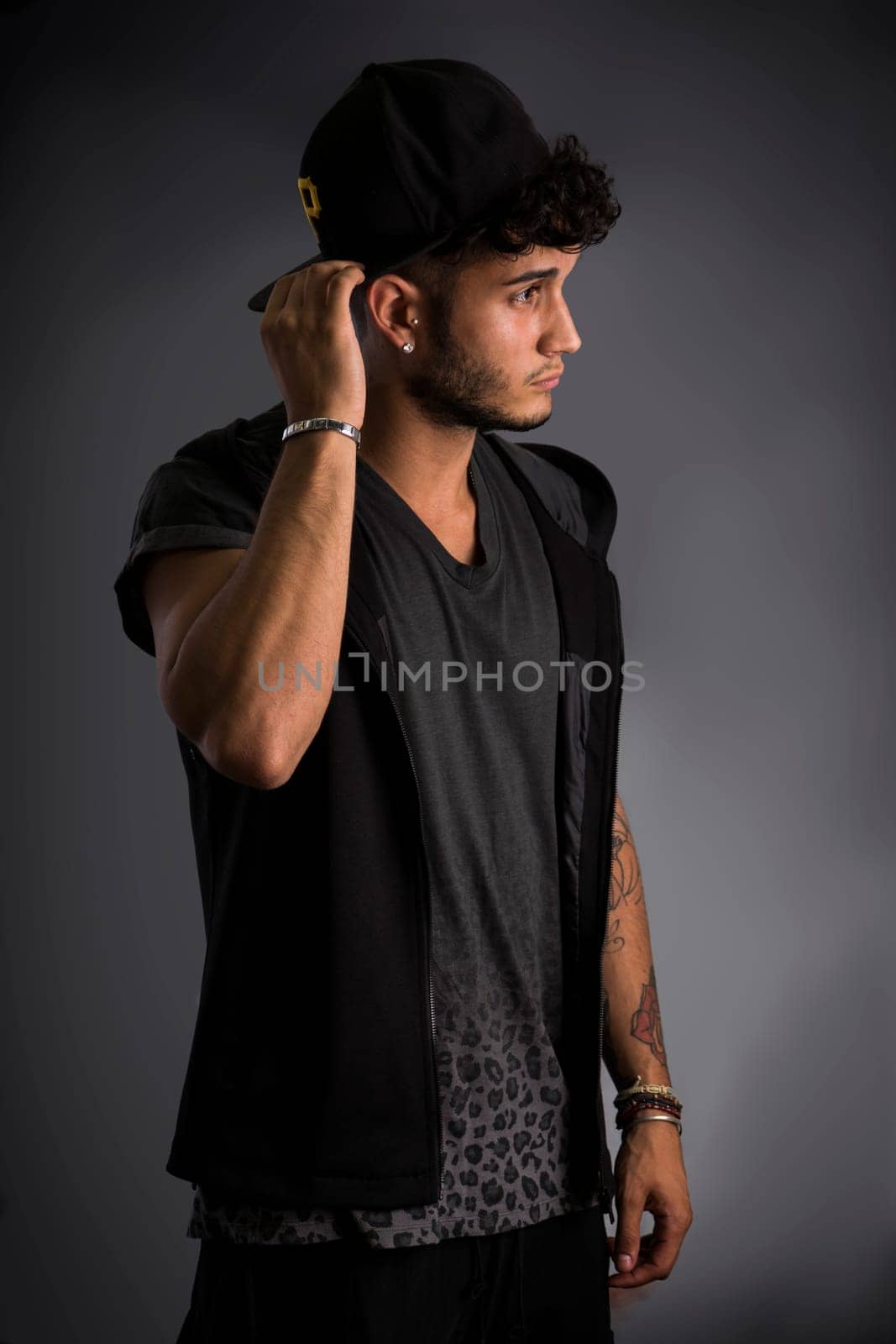 Profile of handsome young man in dark t-shirt and baseball hat, on black background. Looking away