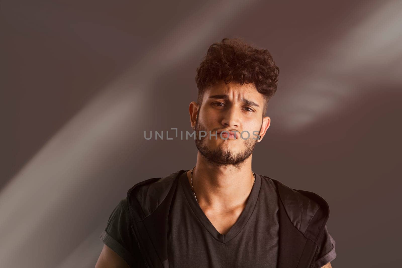 Portrait of handsome young man in dark t-shirt on black background, with an expression of challenge. Looking away