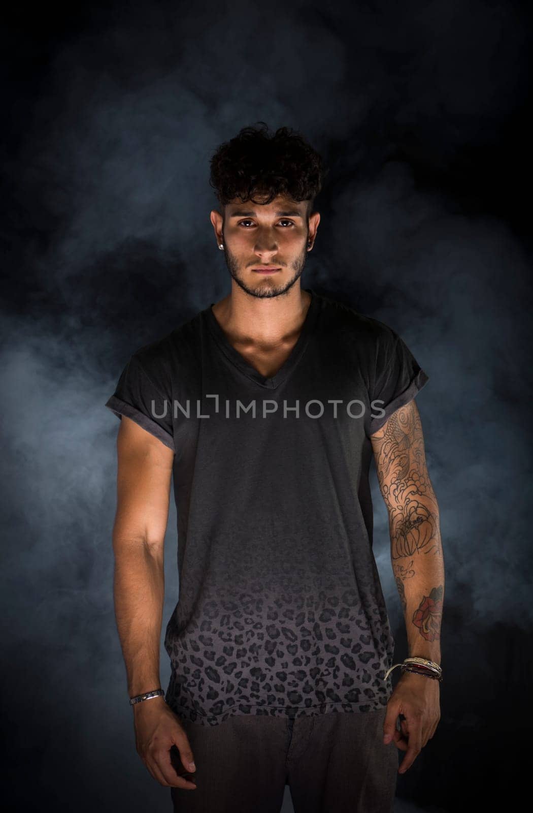 Portrait of handsome young man in dark t-shirt on black background. Dramatic lighting with smoke