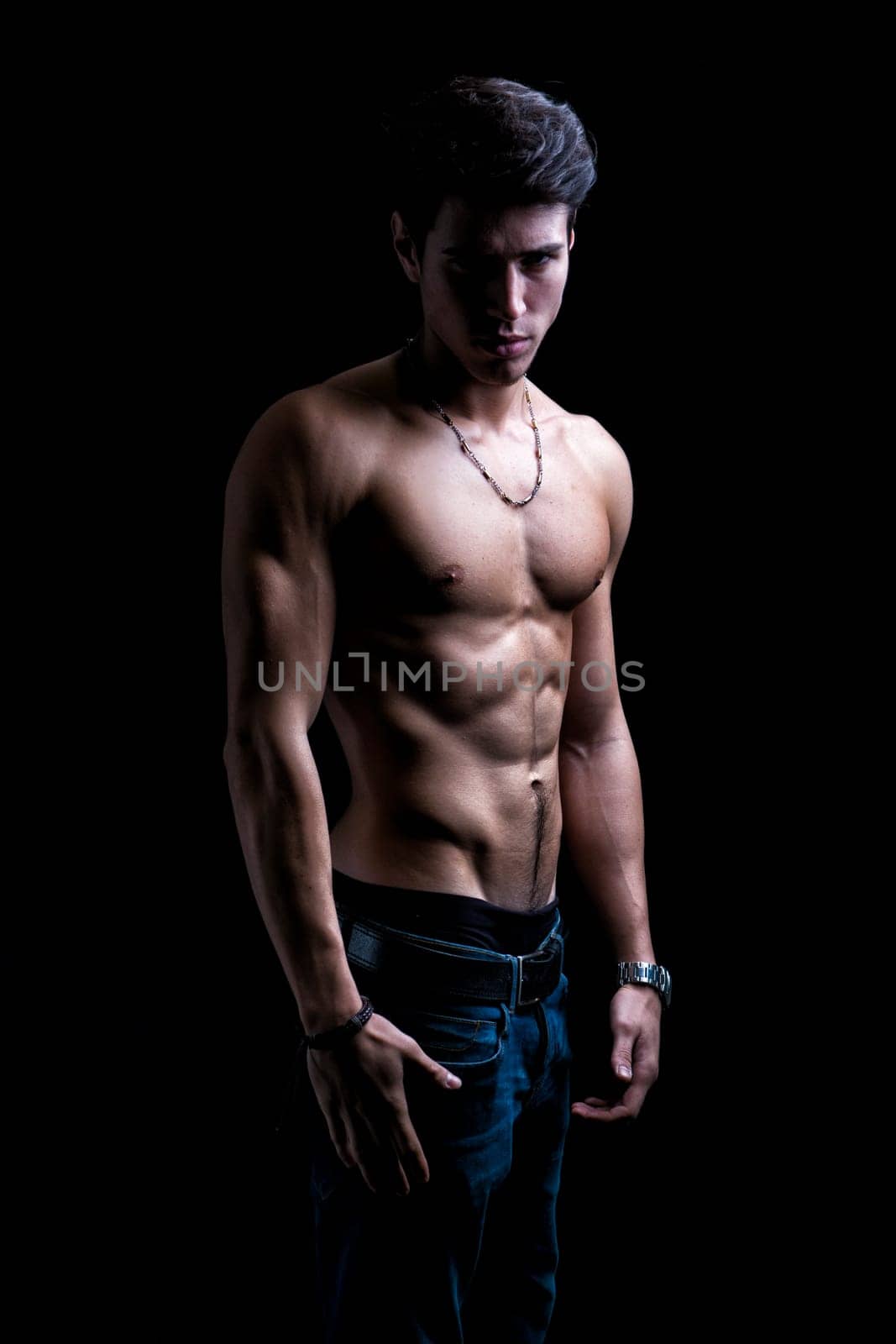 Handsome shirtless muscular young man's profile, looking at camera, on dark background