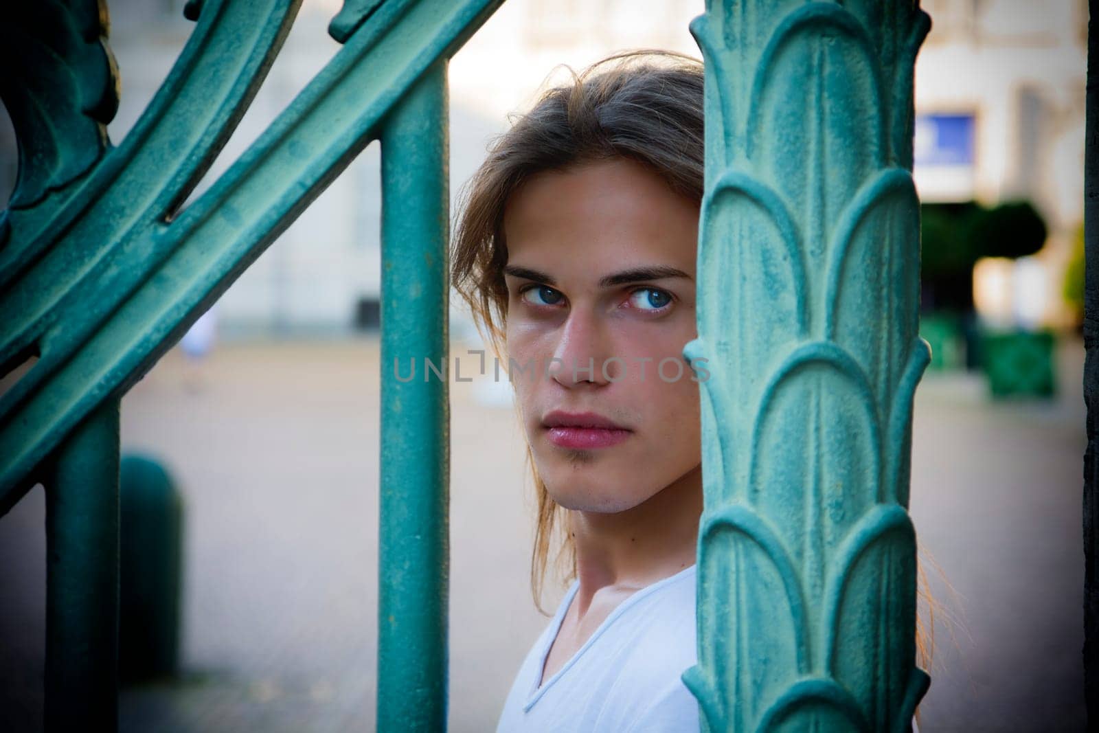 Gorgeous Long Hair Man in White behind Blue Green Art Metal Bars