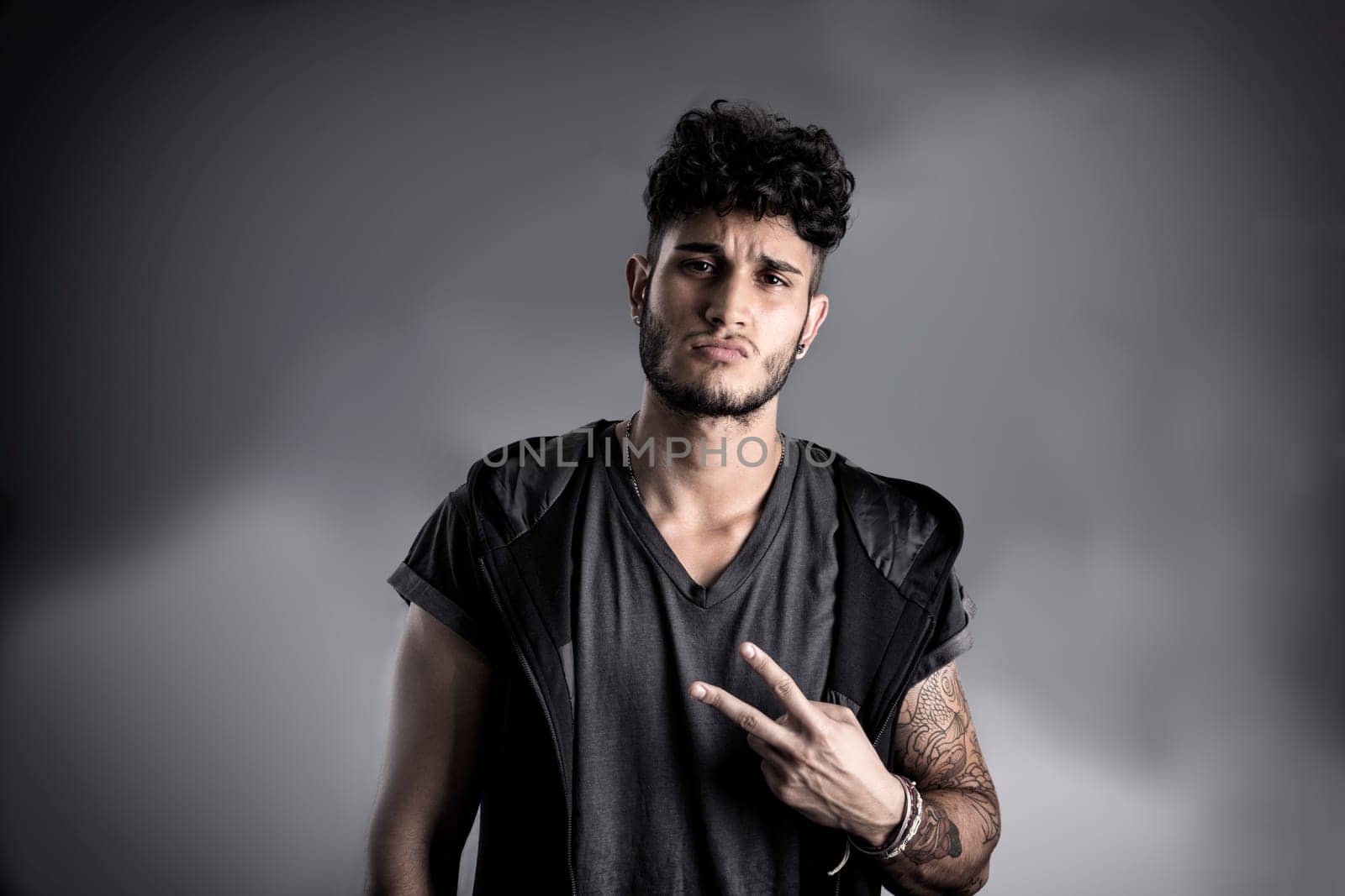 Portrait of handsome young man in dark t-shirt on black background, doing Victory sign with fingers. Looking away