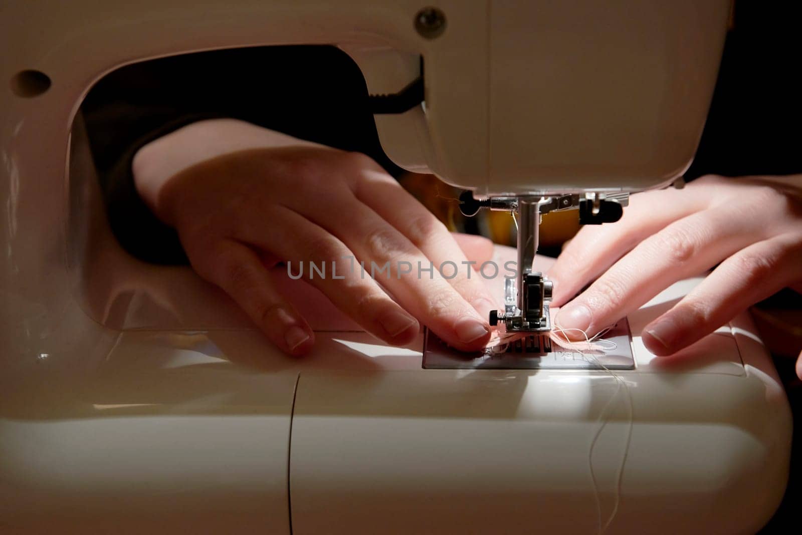 Detail of hands working on piece of fabric on automatic sewing machine