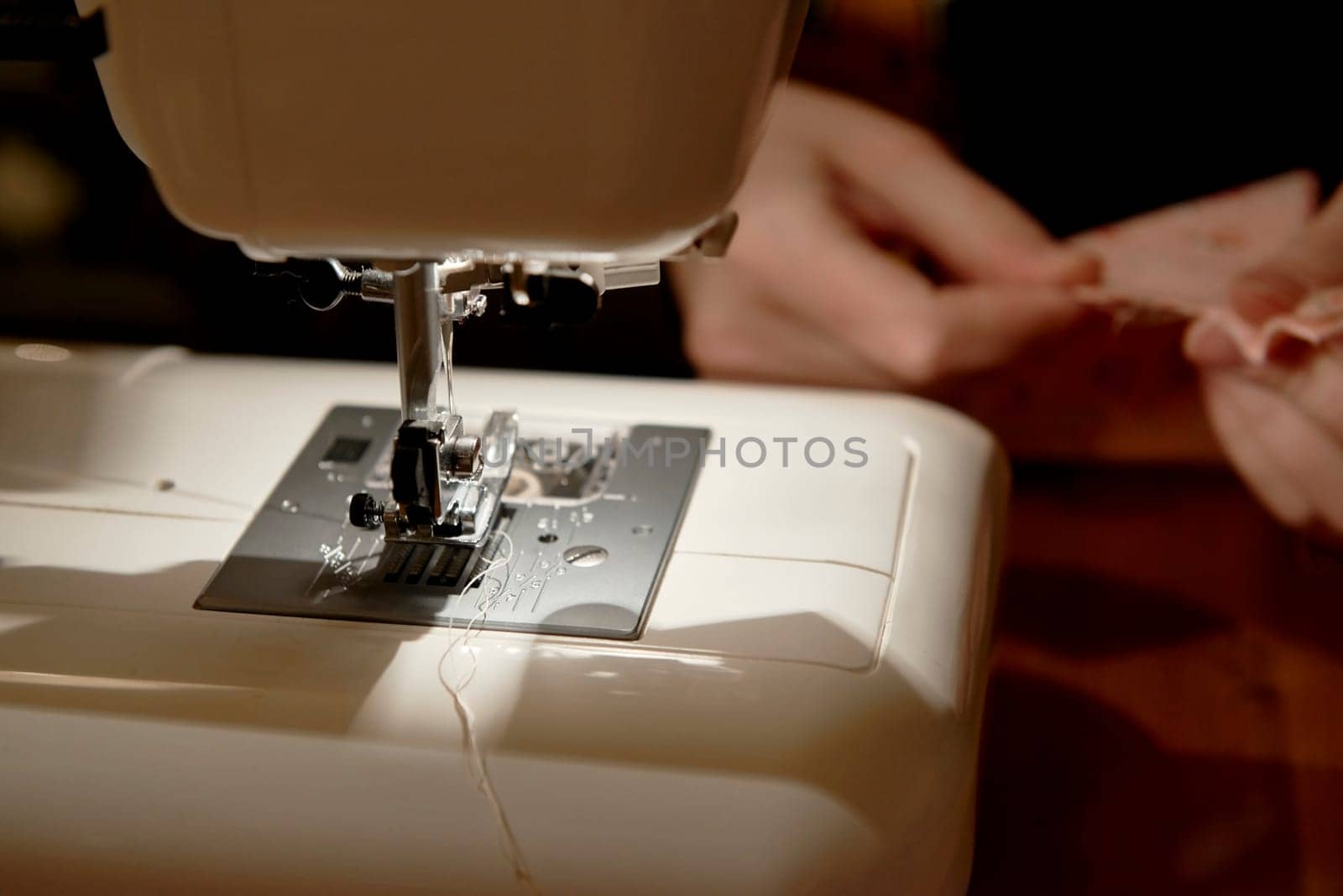 Detail of automatic sewing machine with hands working on piece of fabric in the background