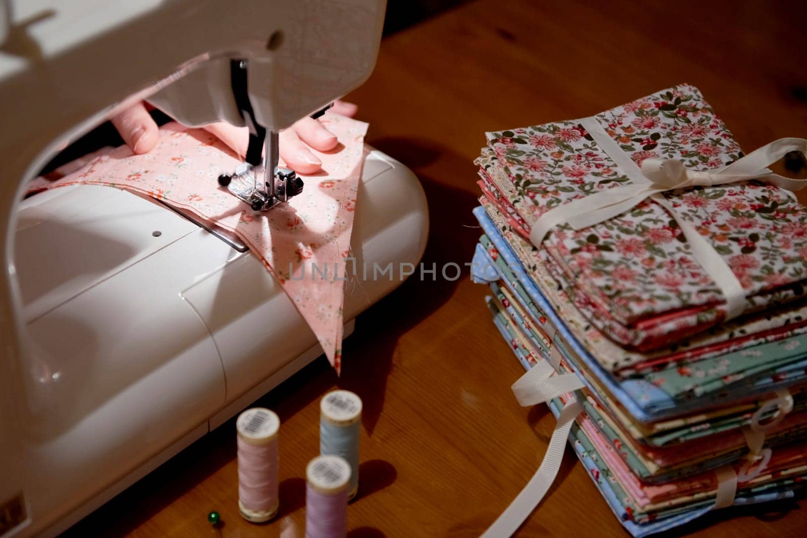 High angle detail of hands working on piece of fabric on automatic sewing machine, with fabric stacked on the side