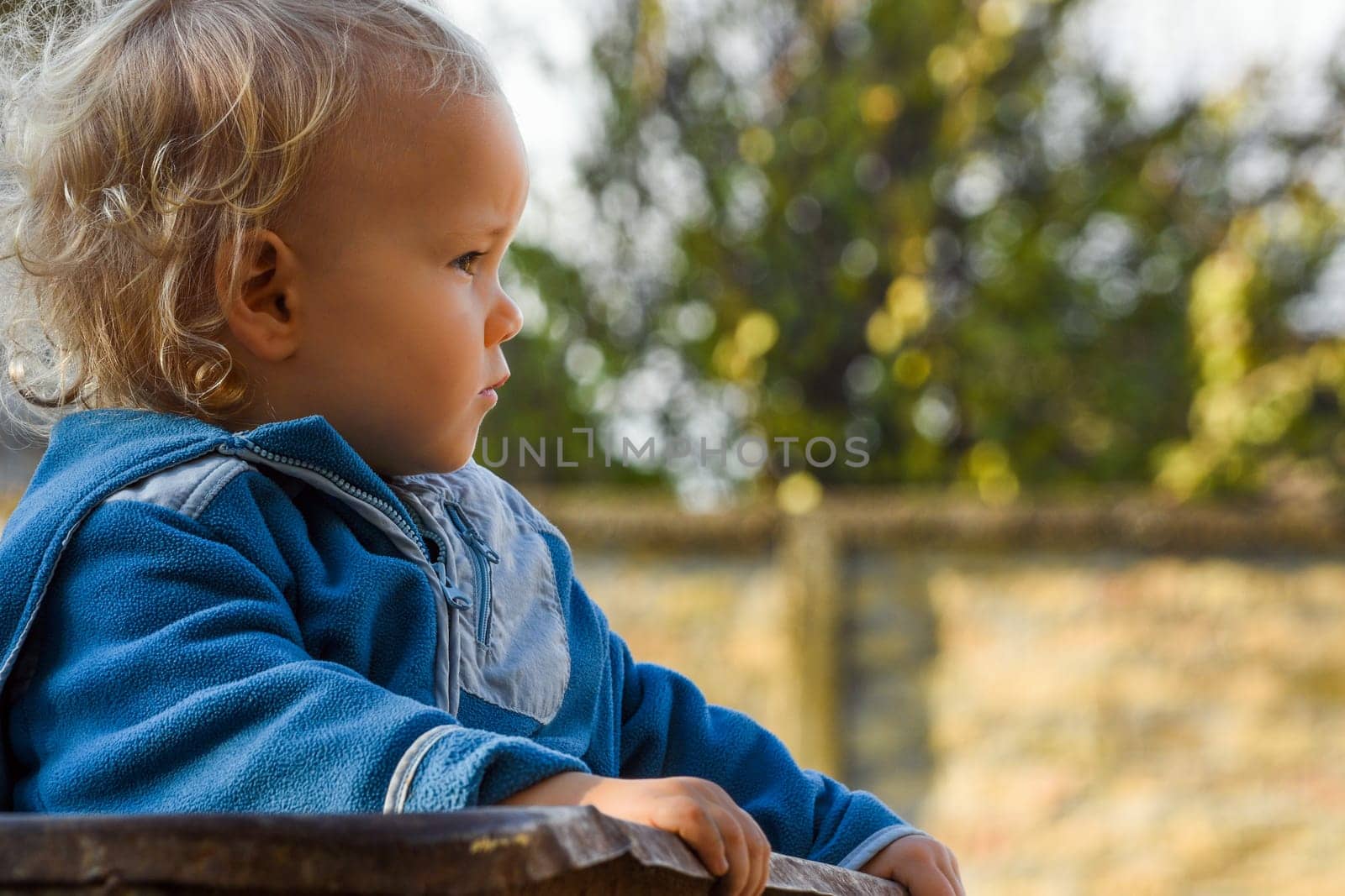 Little child is sitting outdoor and looks away.