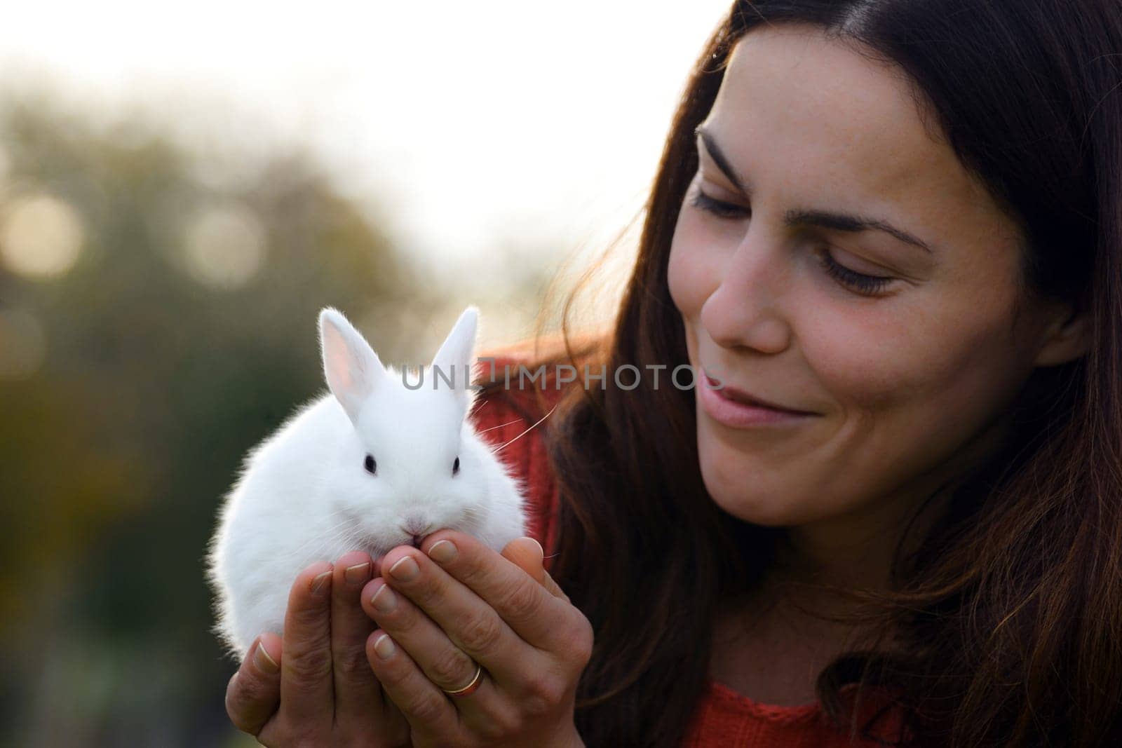 The smiling woman is holding a little cute white bunny.