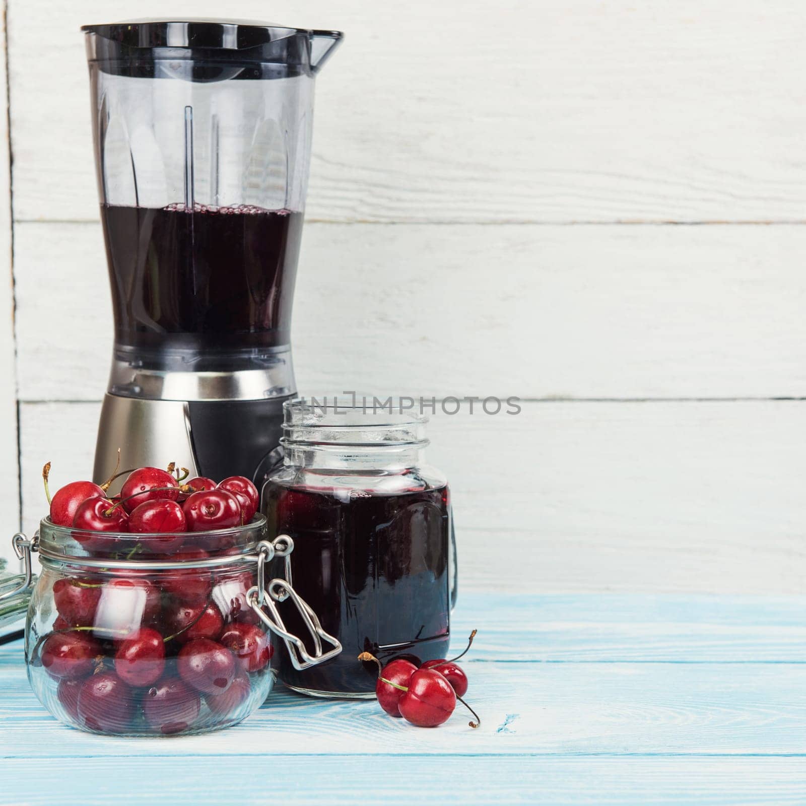 Cherry juice with glass jar,of berries, blender and juice on blue wooden background