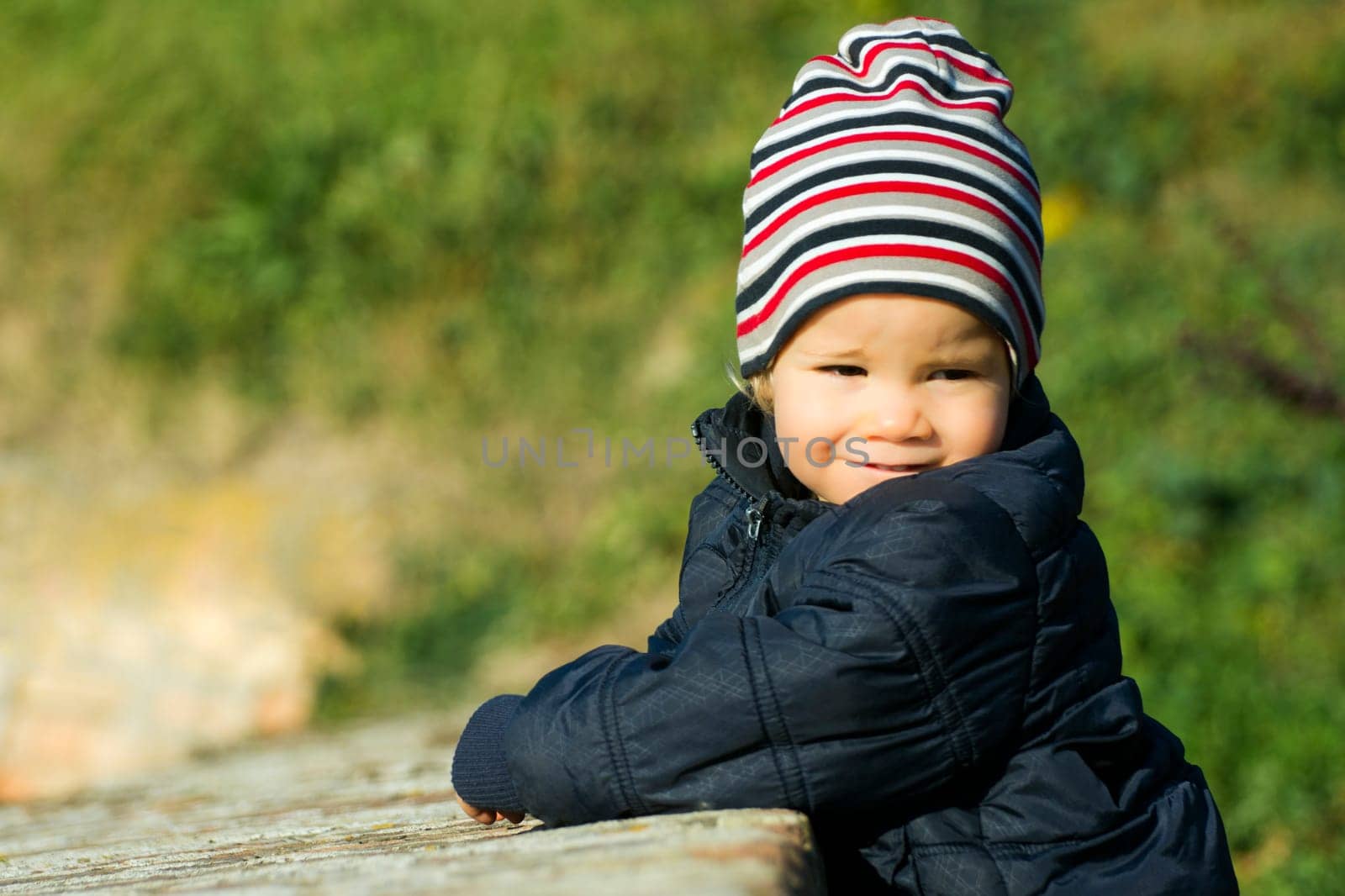 Lovely little boy with striped cap is outdoor on green background.