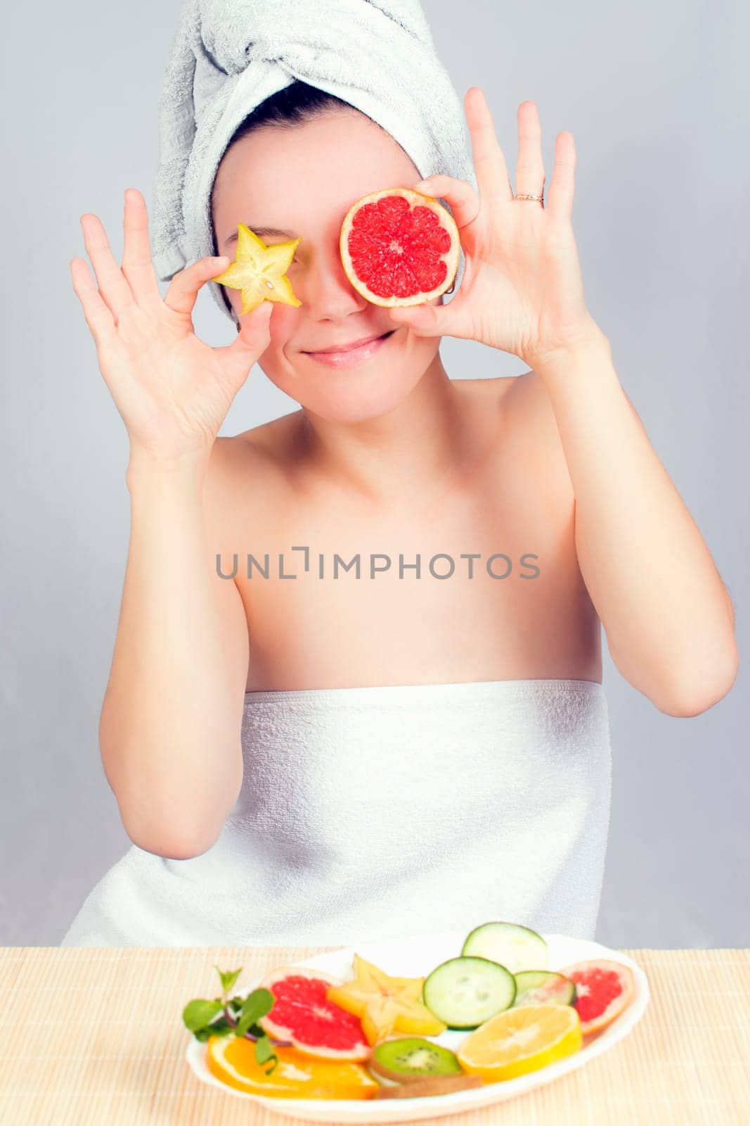 Young woman holds slices of carambola and red grapefruit like her eyes.