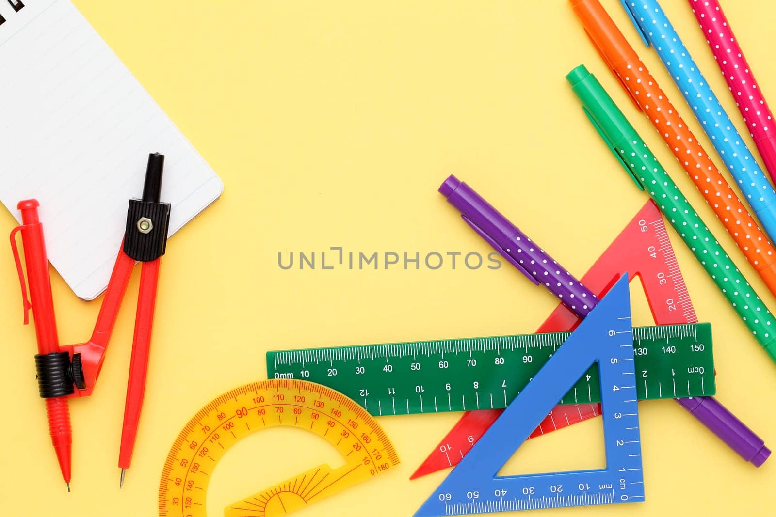 Multicolored pen, rulers and notebook on yellow background