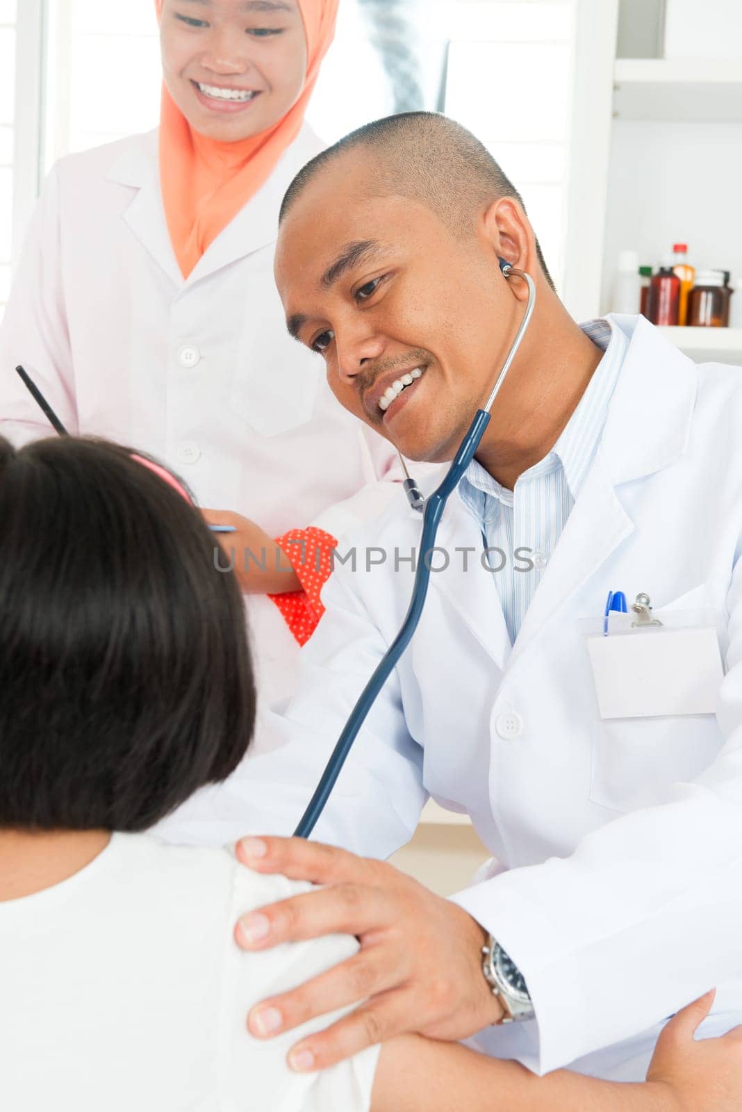 Asian children's doctor exams child with stethoscope.