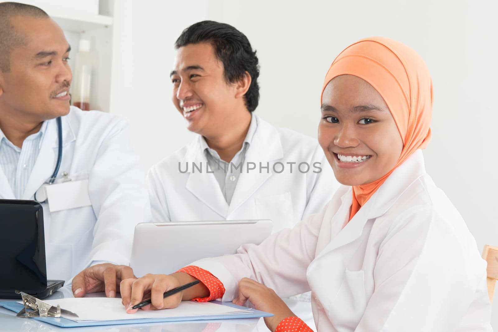 Asian medical doctors having discussion on desk inside hospital room.