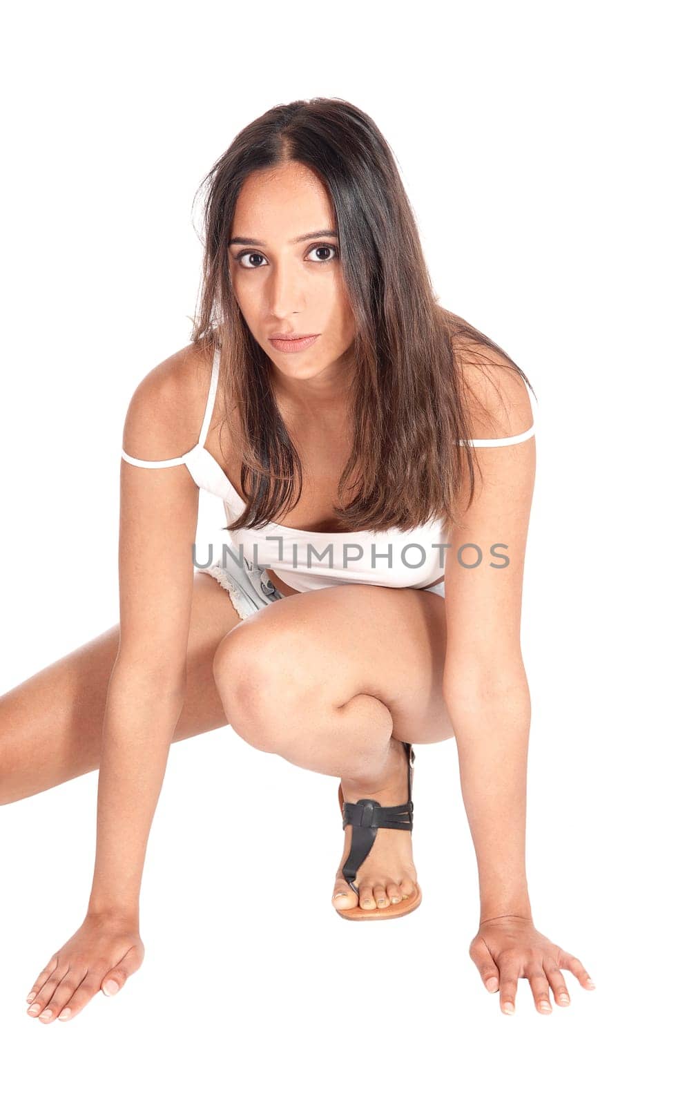 A beautiful young woman in shorts and sandals crouching on the floor,.looking into the camera, isolated for white background..