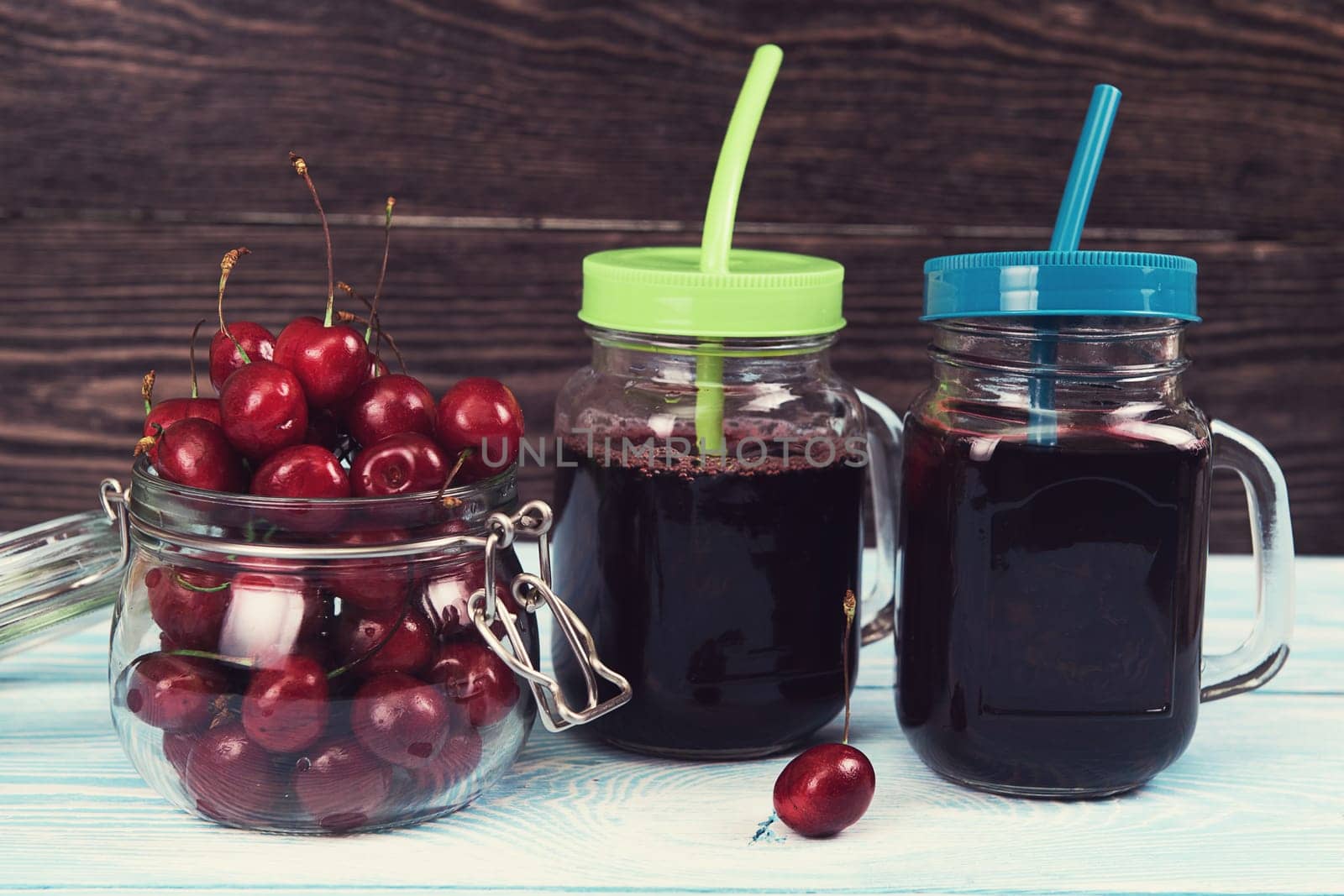 Cherry juice with glass jar of berries on blue wooden background