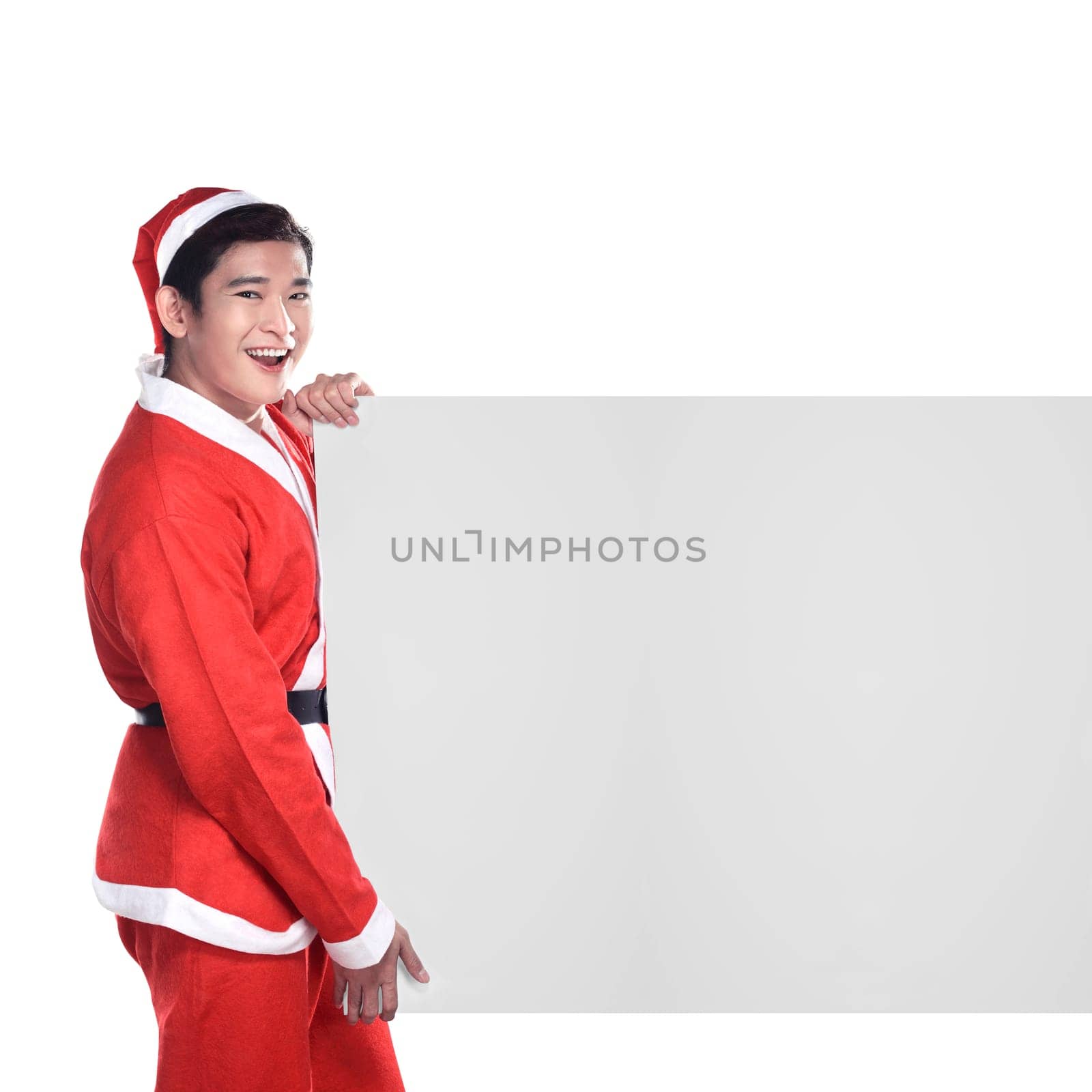 Young man in Santa Claus costume behind white board with space for text over white background