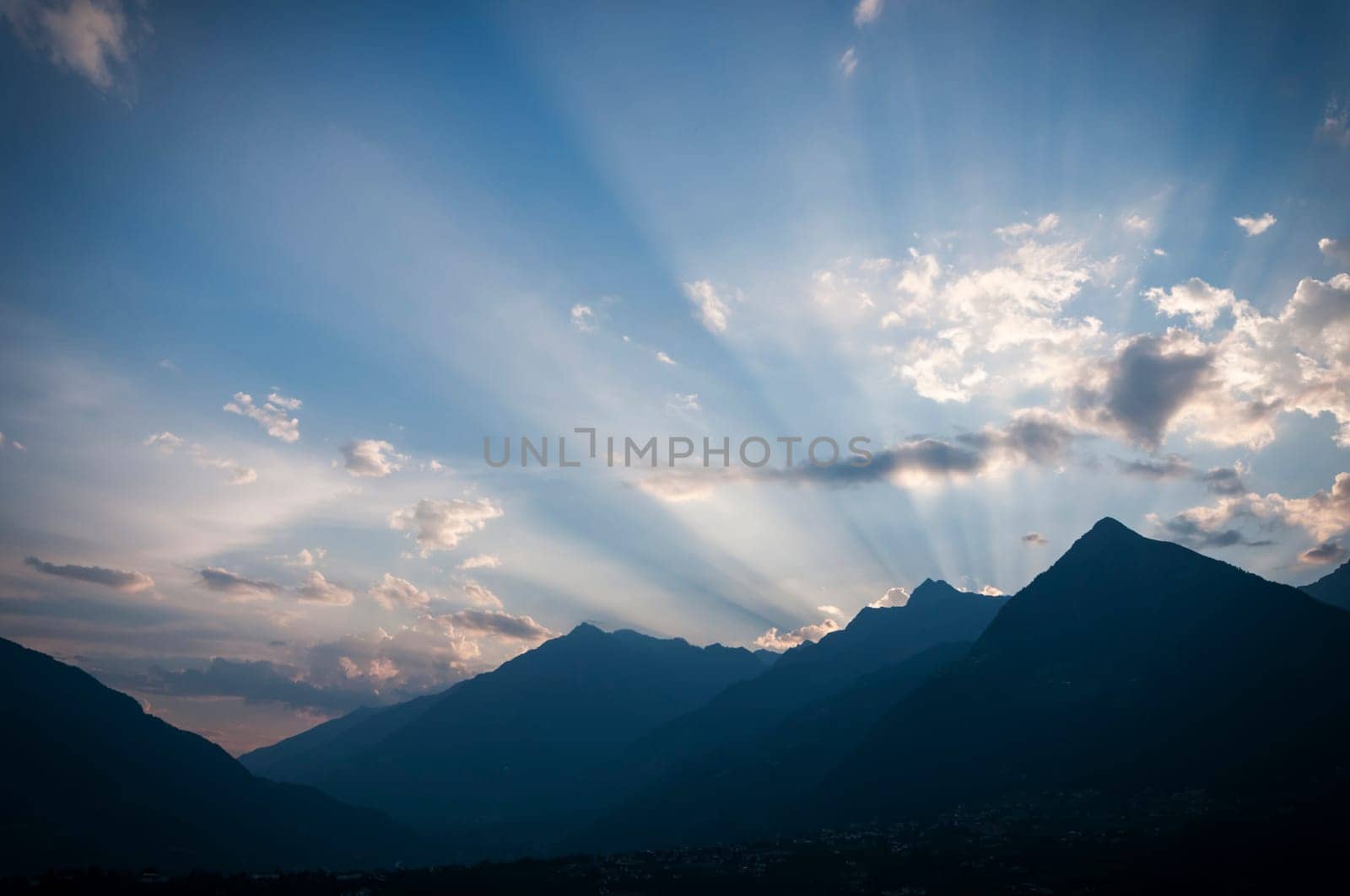 The sun setting behind the mountains of South Tyrol shines on individual clouds in the evening sky.