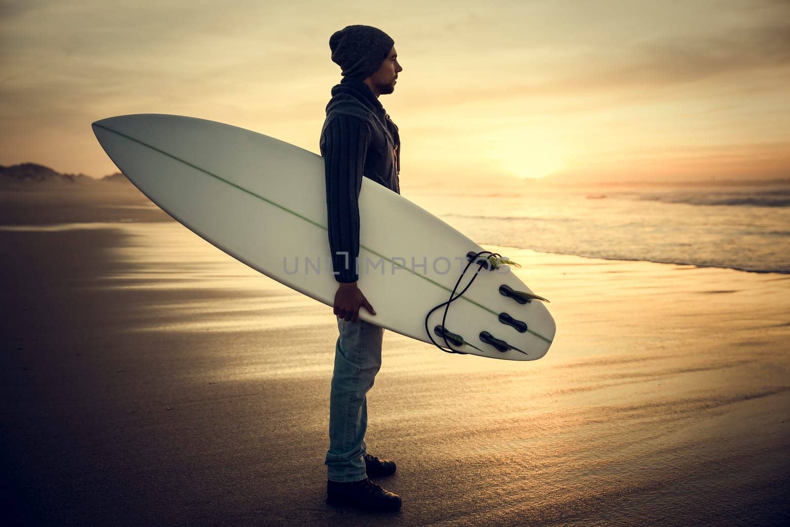 A surfer with his surfboard at the sunset looking to the waves