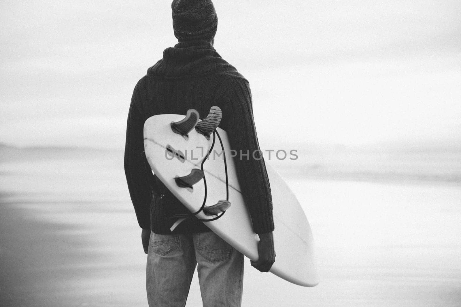 A surfer with his surfboard at the sunset looking to the waves