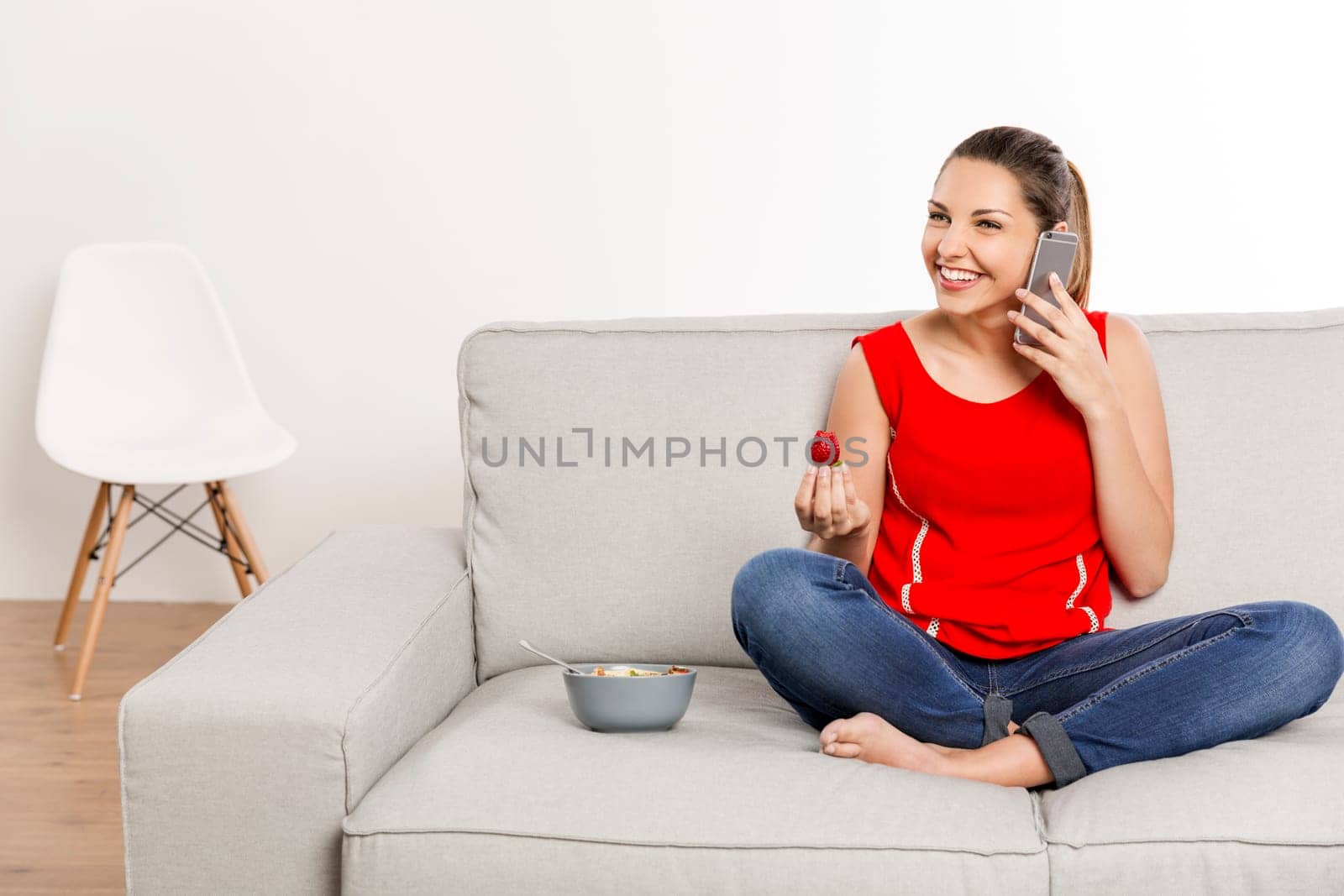 Beautiful happy woman at home making a phone call while eating strawberries