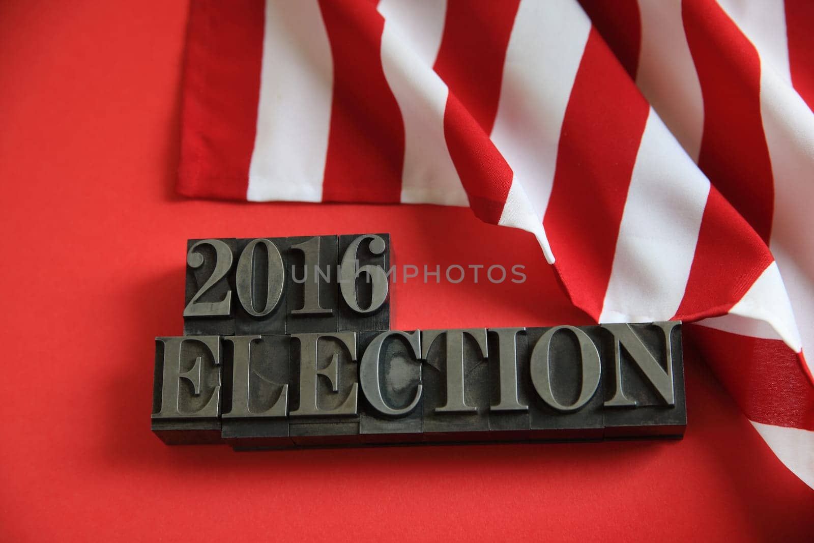 Part of an American flag with 2016 election words in metal type on a red background