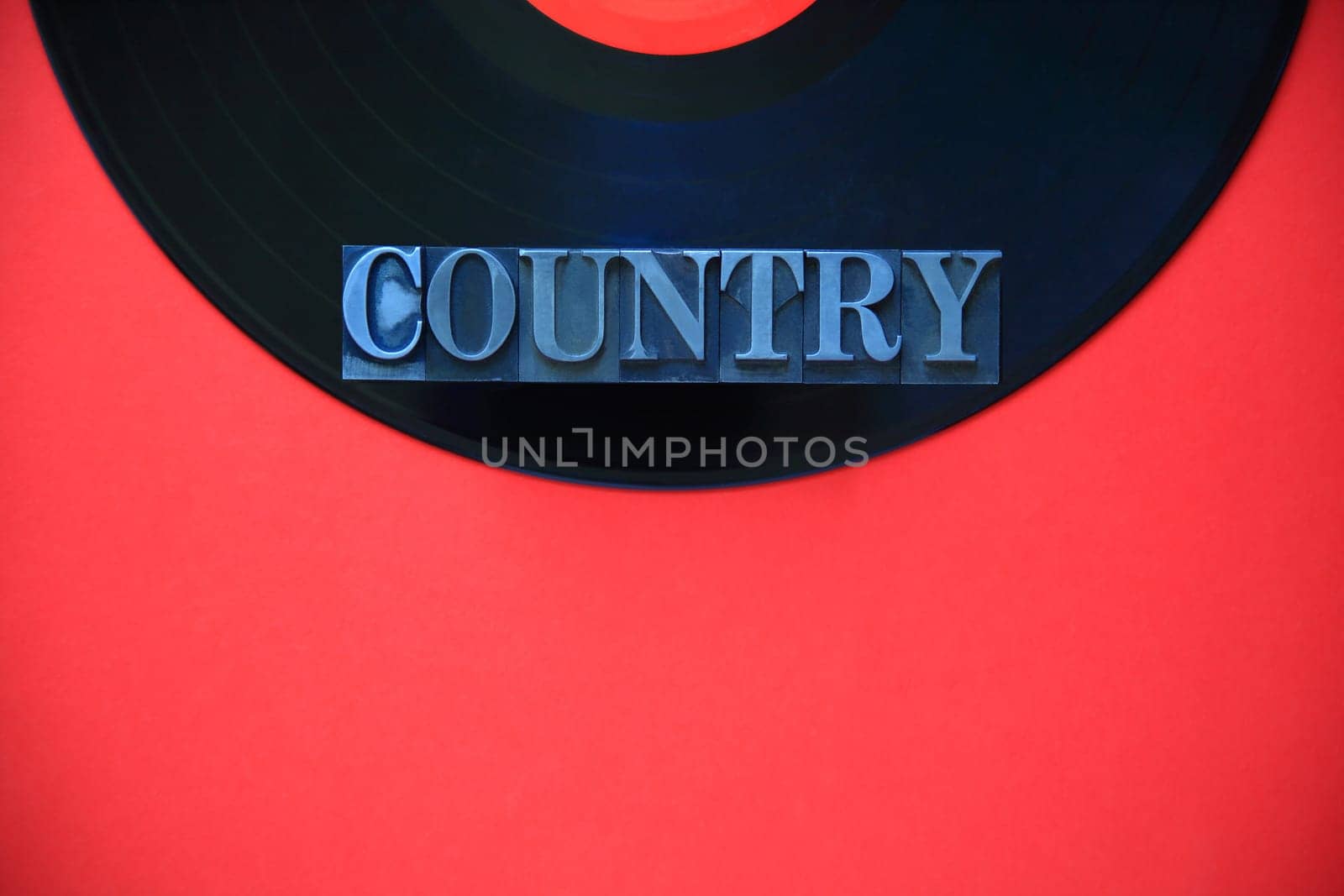 The word country in metal type on a black vinyl record on a red background with copy space