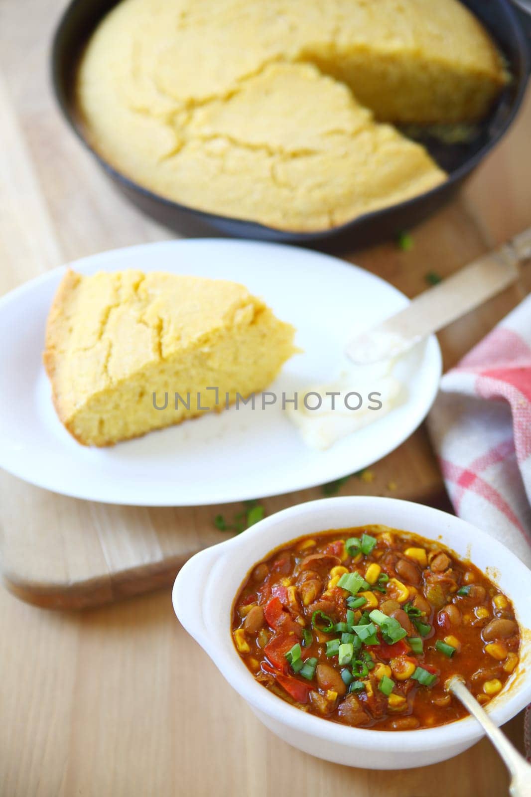 A bowl of chili with wedge of cornbread and butter