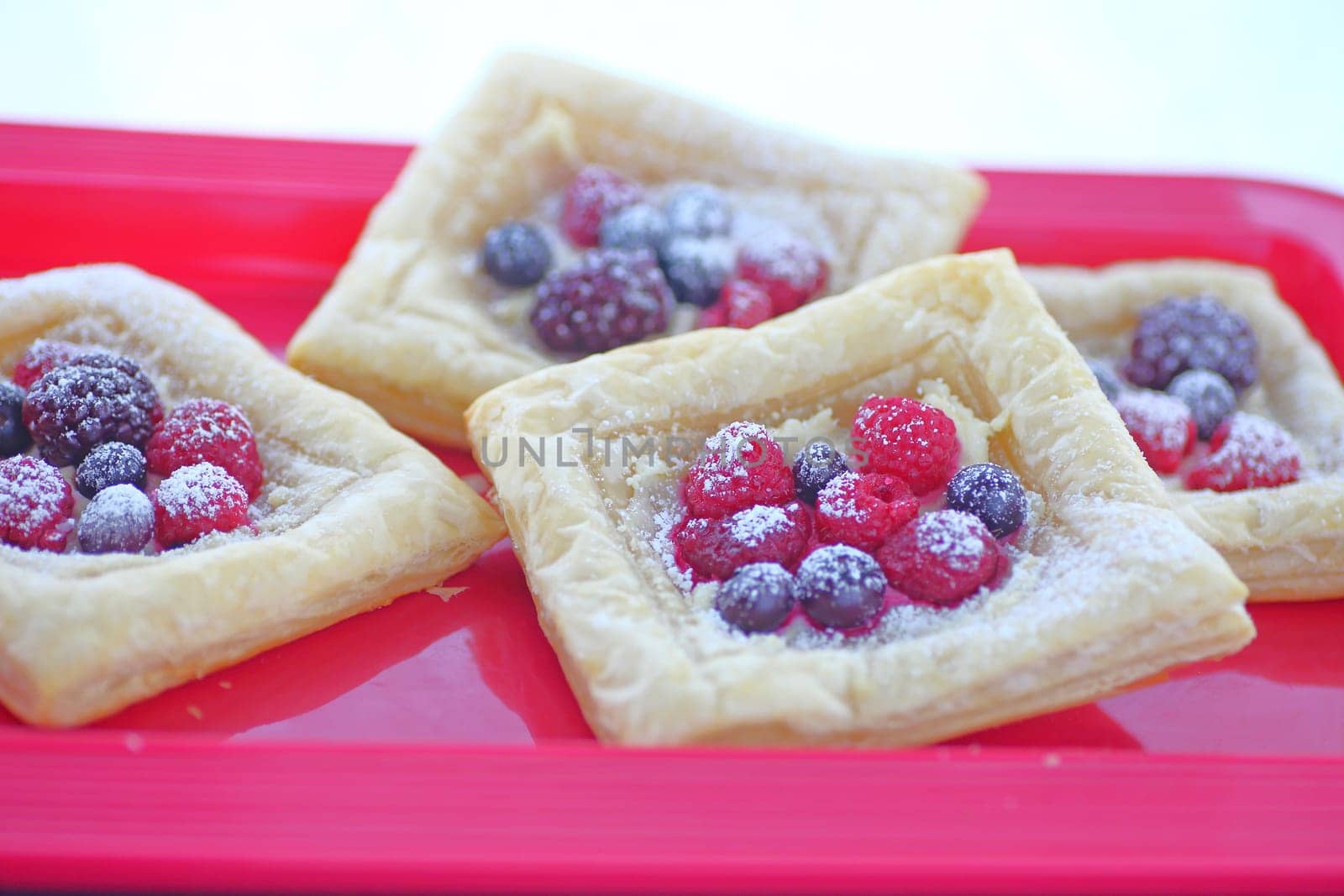 Fresh raspberry, blueberry and blackberry pastries on a red tray