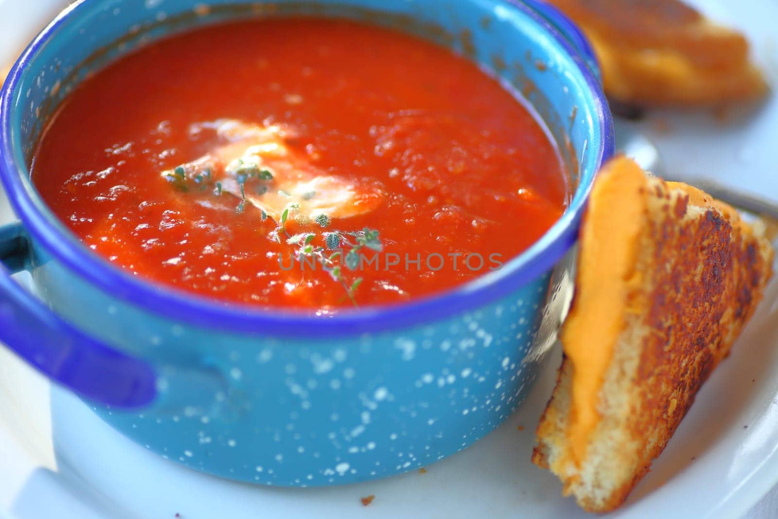 Tomato soup with fresh thyme in an enamelware bowl with a grilled cheese sandwich cut in triangles