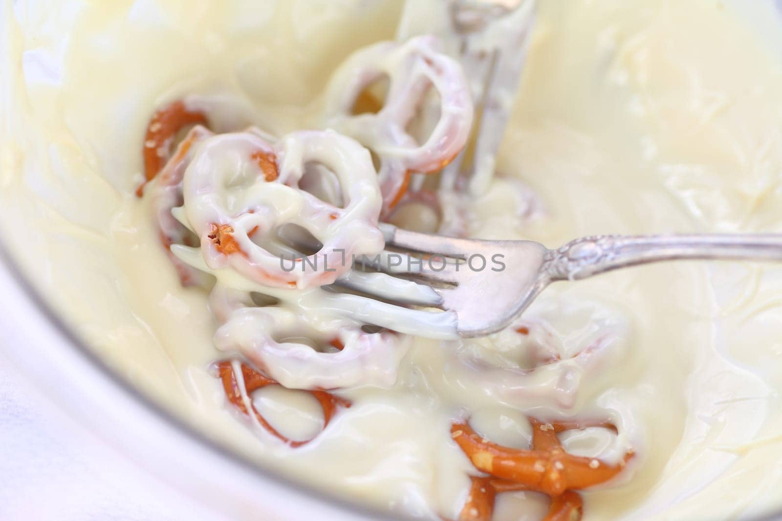 Coating miniature pretzels with melted white chocolate using a fork