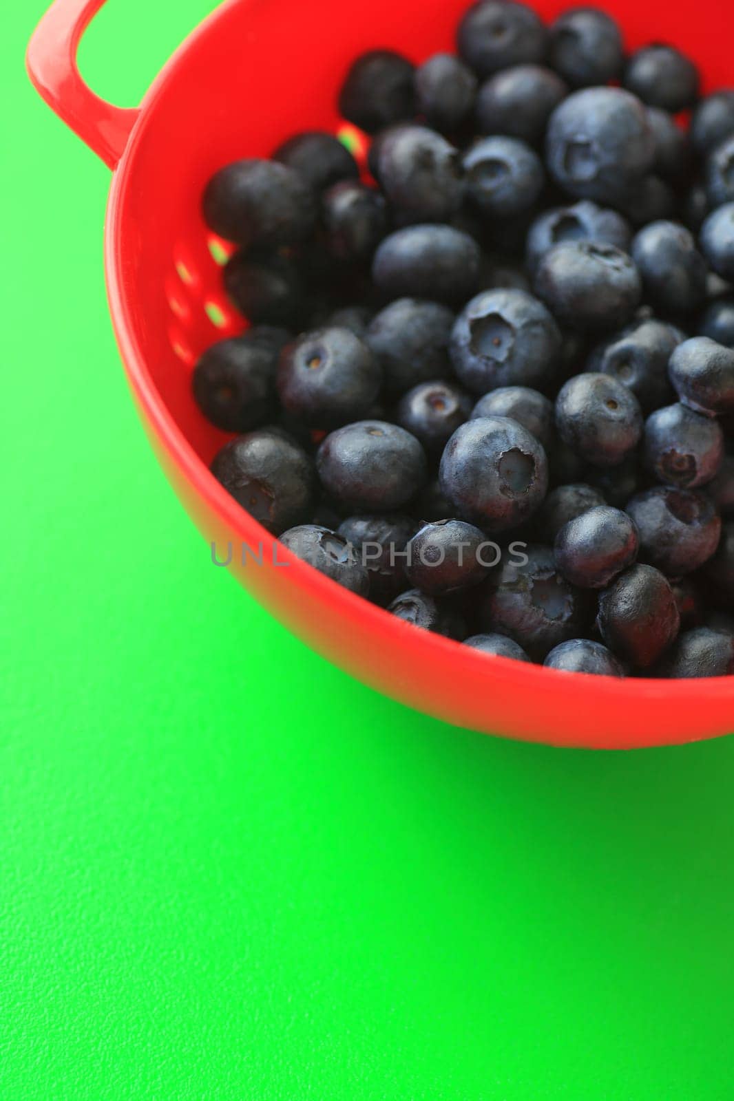 Blueberries in a red colander on a vibrant green background with copy space
