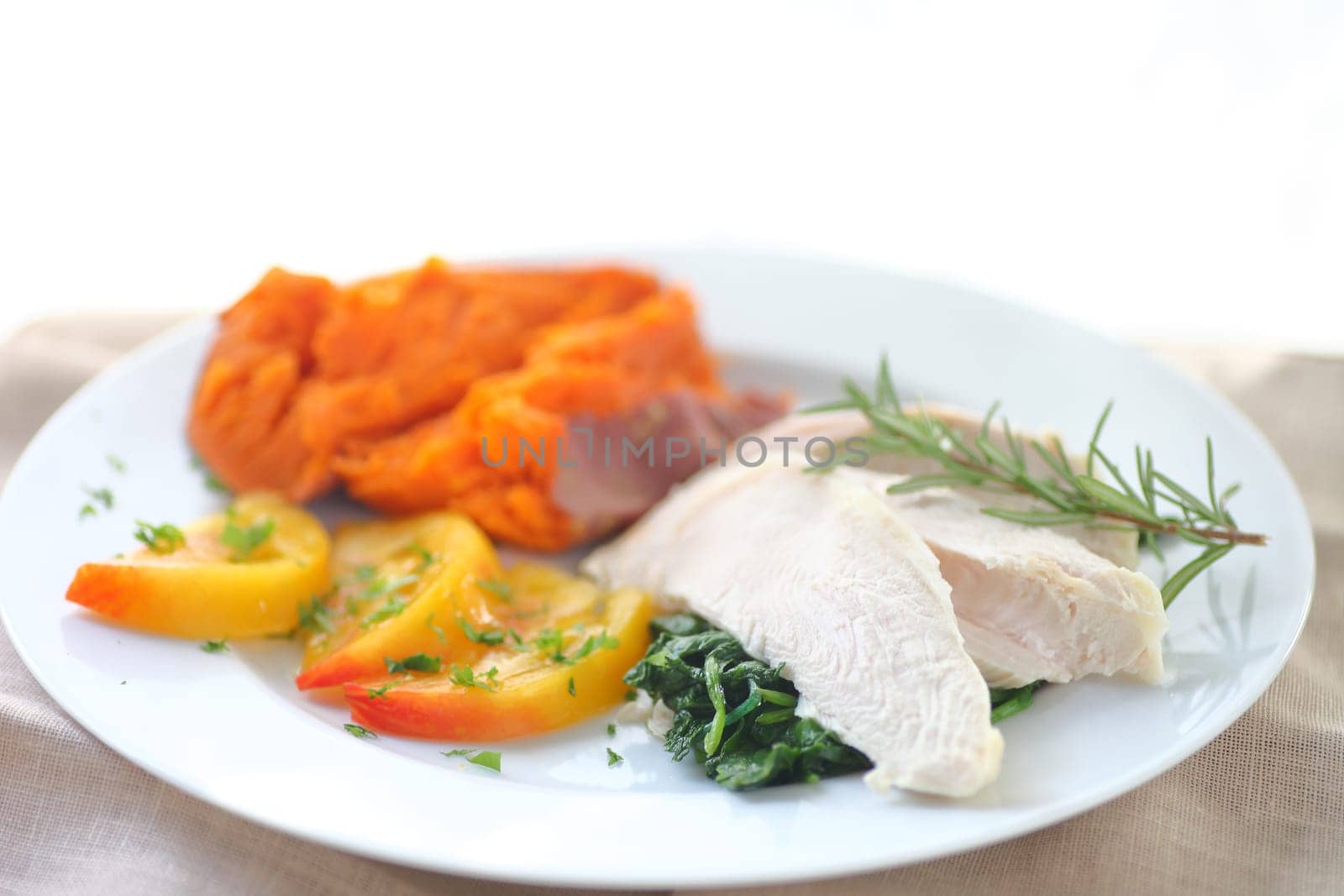 Closeup of poached chicken breast slices on baby kale with baked sweet potato and heirloom tomatoes