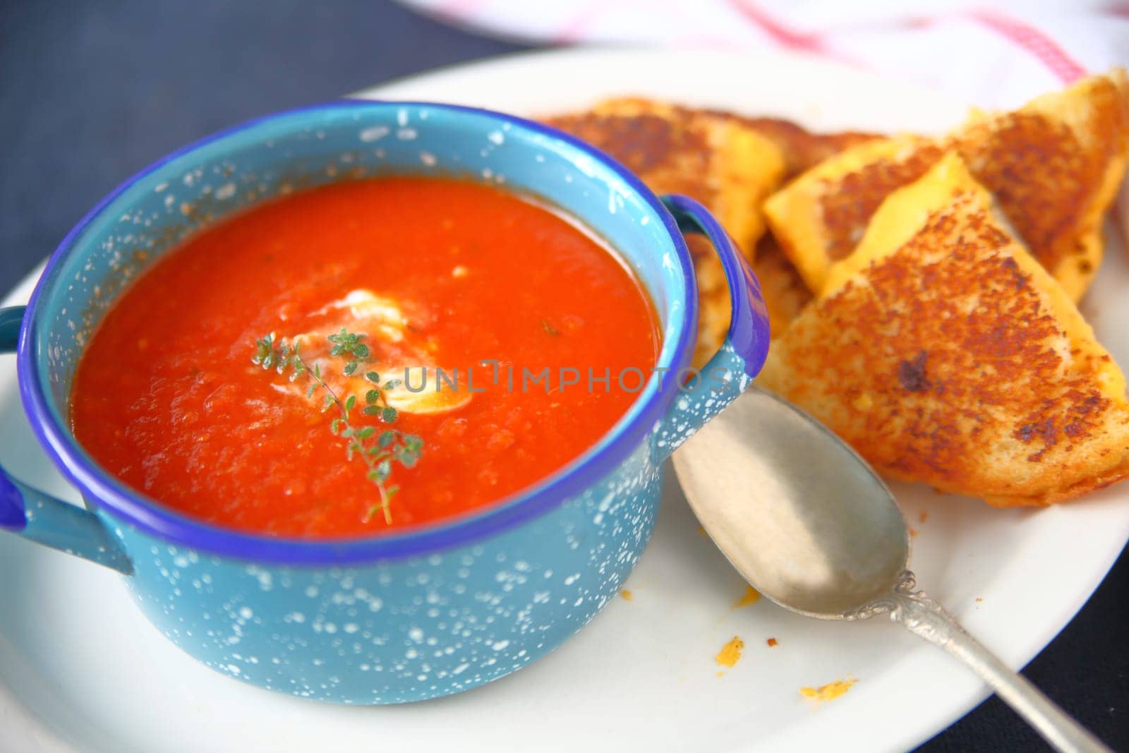 Blue bowl of tomato soup with fresh thyme and a grilled cheese sandwich cut into triangles